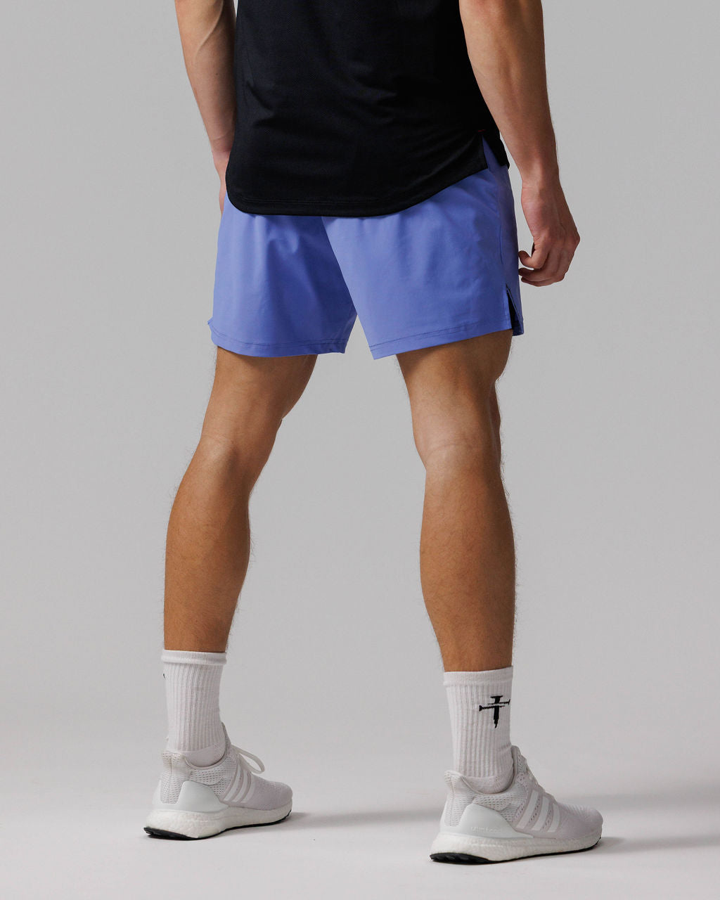 Man wearing Vapor-Lite Liner Short Cross in Serene Blue, back view, paired with black tee and white sneakers.