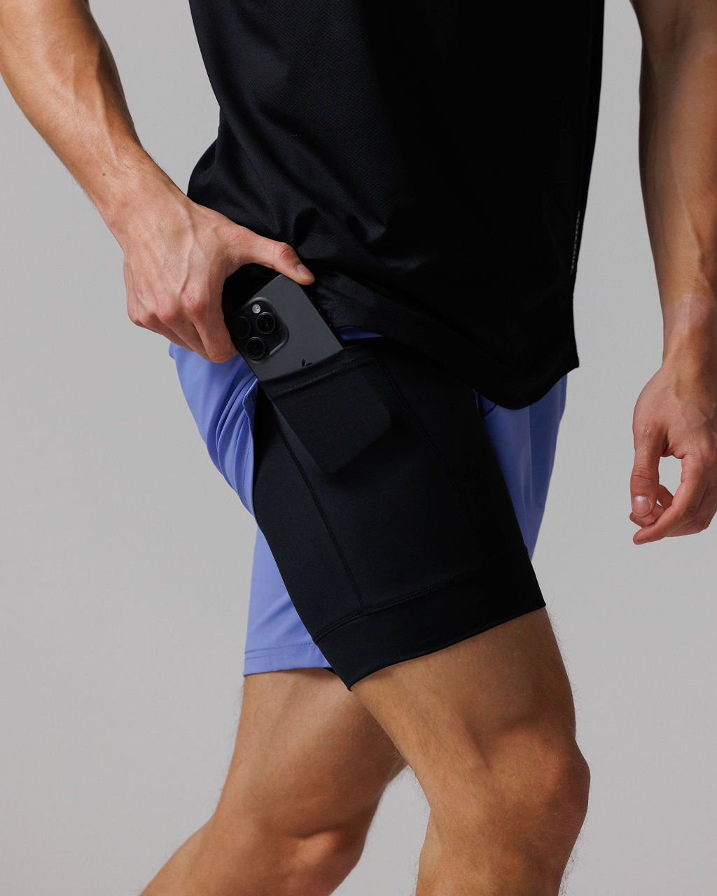 Side angle close-up of Vapor-Lite Liner Short Cross in Serene Blue showing phone pocket detail with model inserting a smartphone.