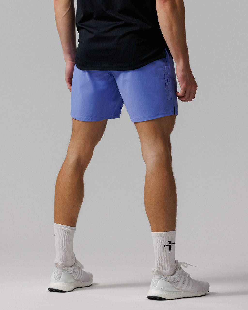 Back view of model wearing Vapor-Lite Hybrid Short in Serene Blue with perforated side detail, paired with white sneakers.