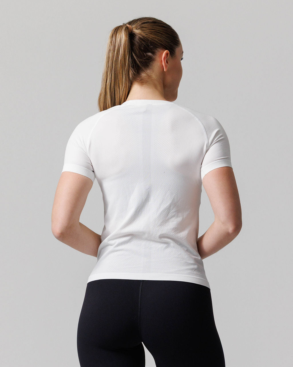 Women's Seamless Tee Cross in white, back view on model wearing black leggings with hair in ponytail.