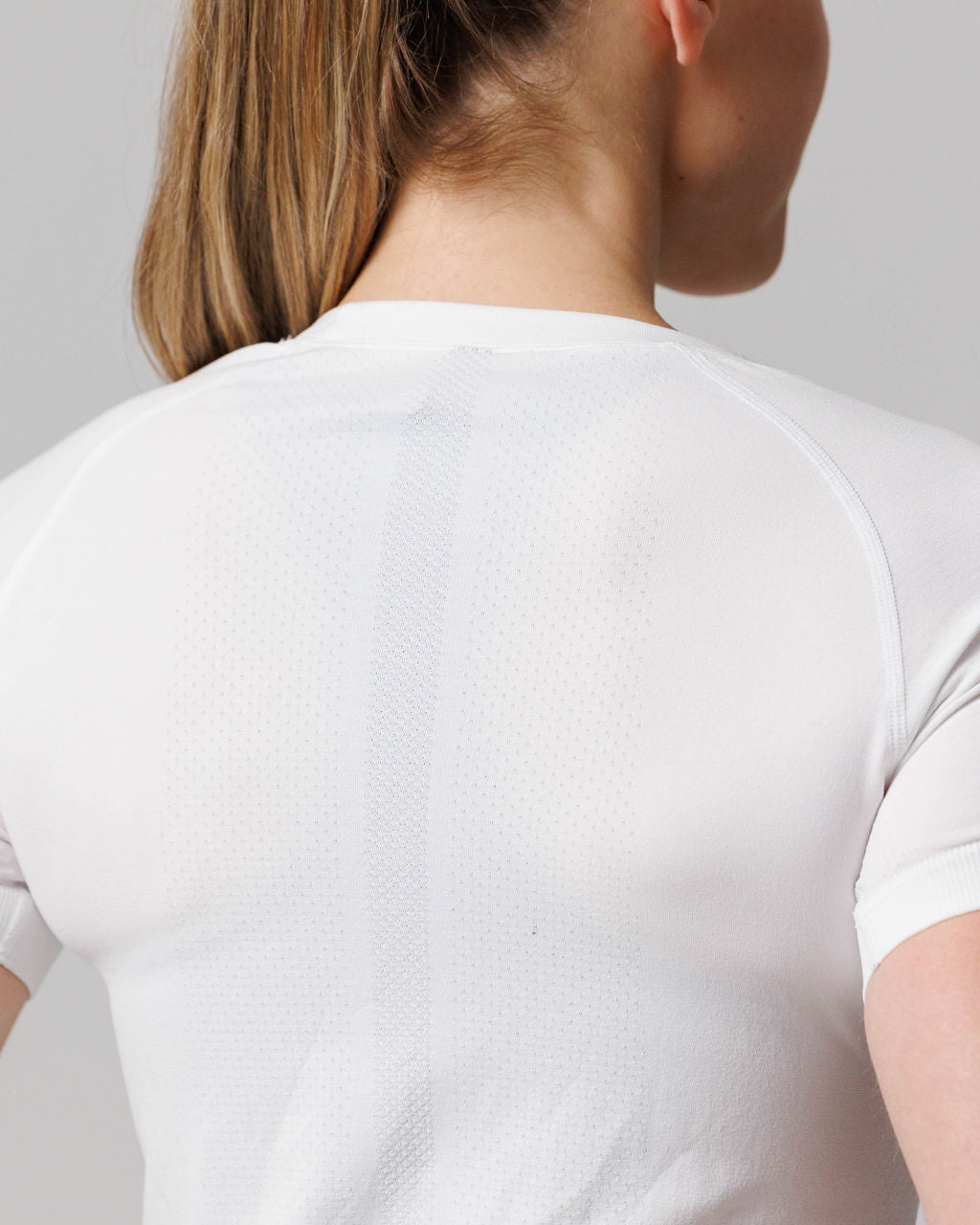 Back view close-up of womens seamless tee Cross in white showing textured cross detail on upper back.