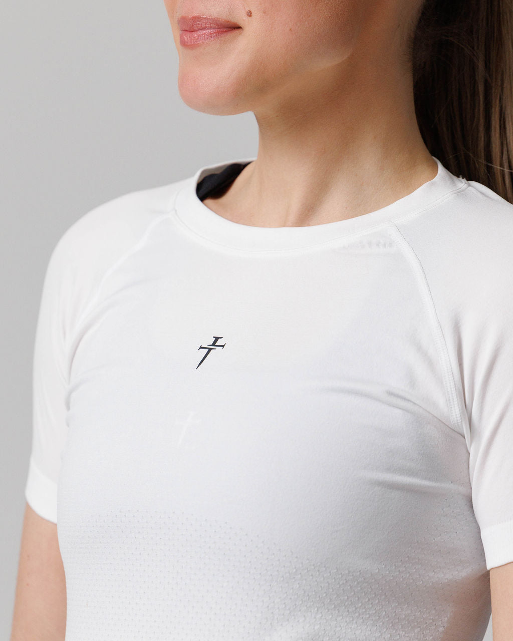 Close-up of Women's Seamless Tee Cross in white showing chest logo detail and neckline on a model.