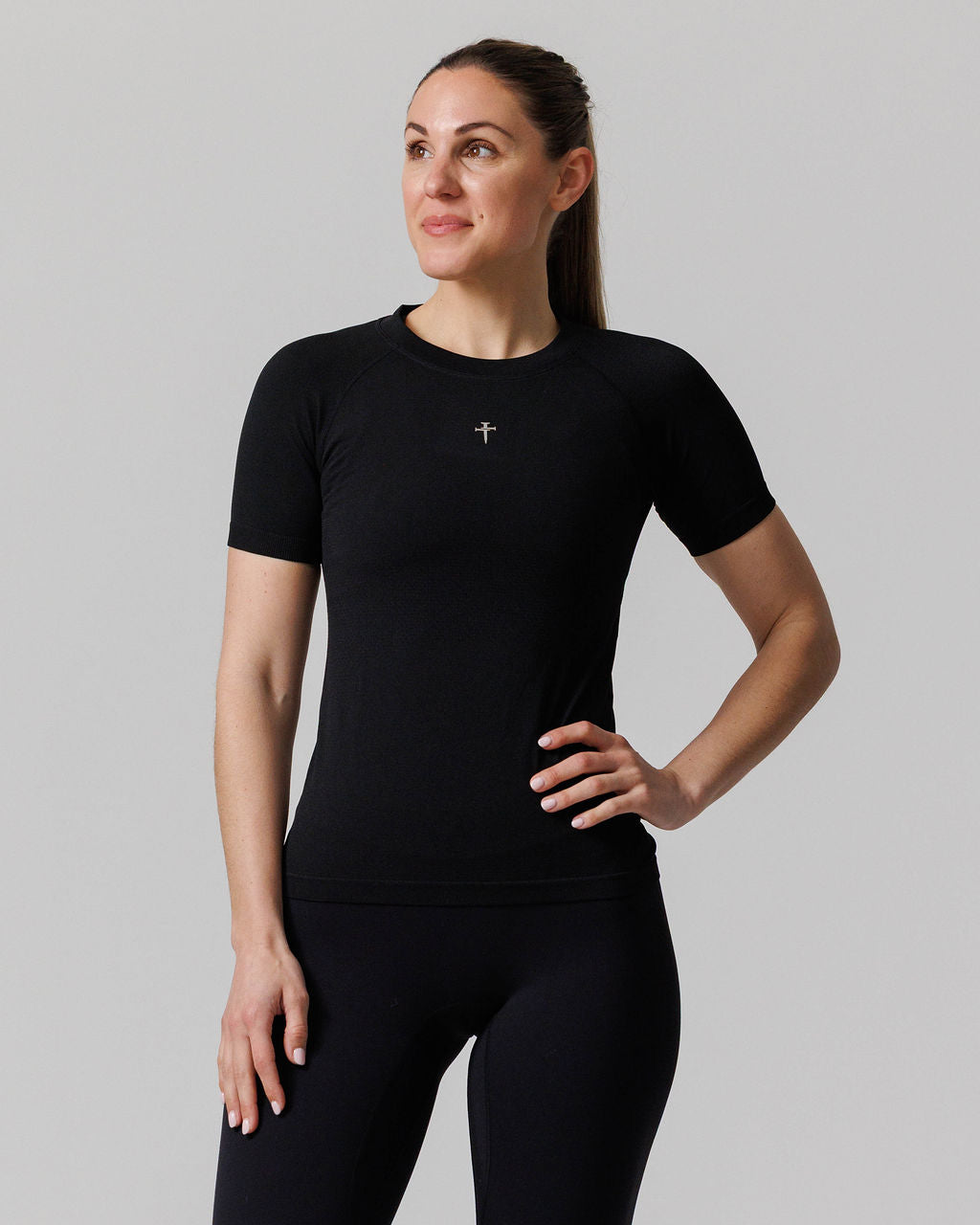Women's Seamless Tee Cross in black, front view on model with hand on hip, small cross logo at chest.