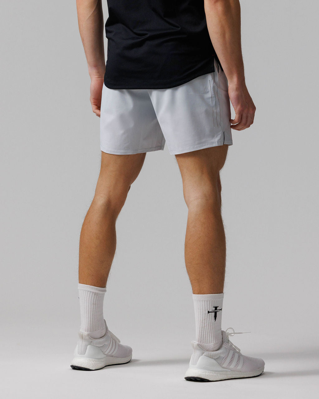 Back view of model wearing Vapor-Lite Hybrid Short in Stone with perforated side details, paired with white sneakers.