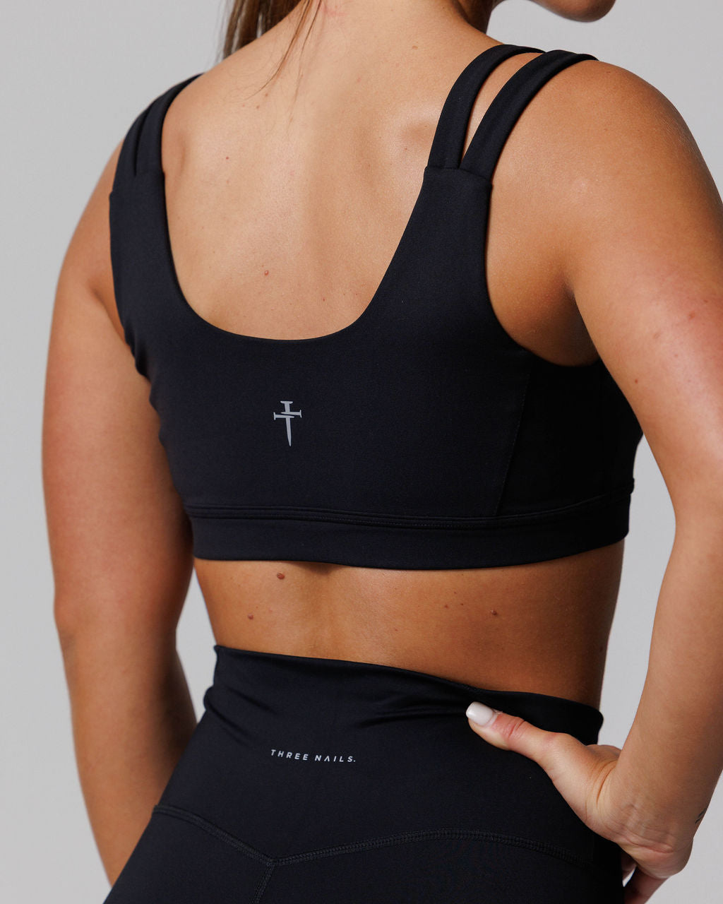 Back view of the Nova Split-Strap Sports Bra in black, showing double straps and Three Nails logo on a model.