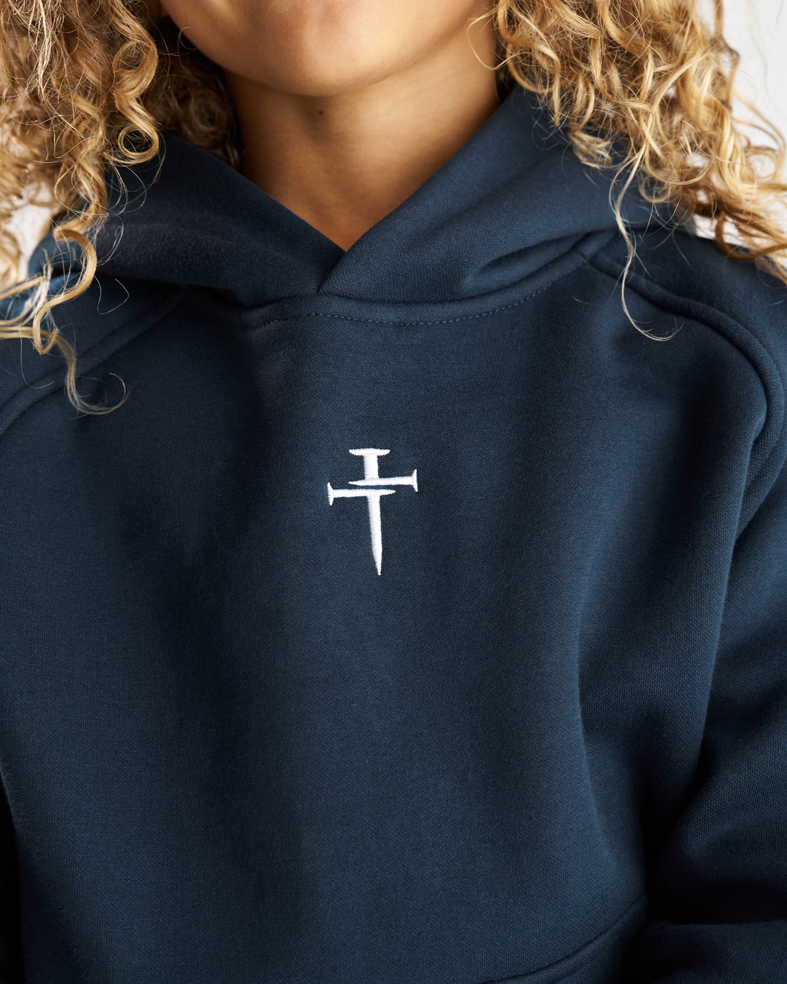 Close-up of Youth Signature Fleece Hoodie in Midnight Navy showing embroidered nail cross logo on chest.