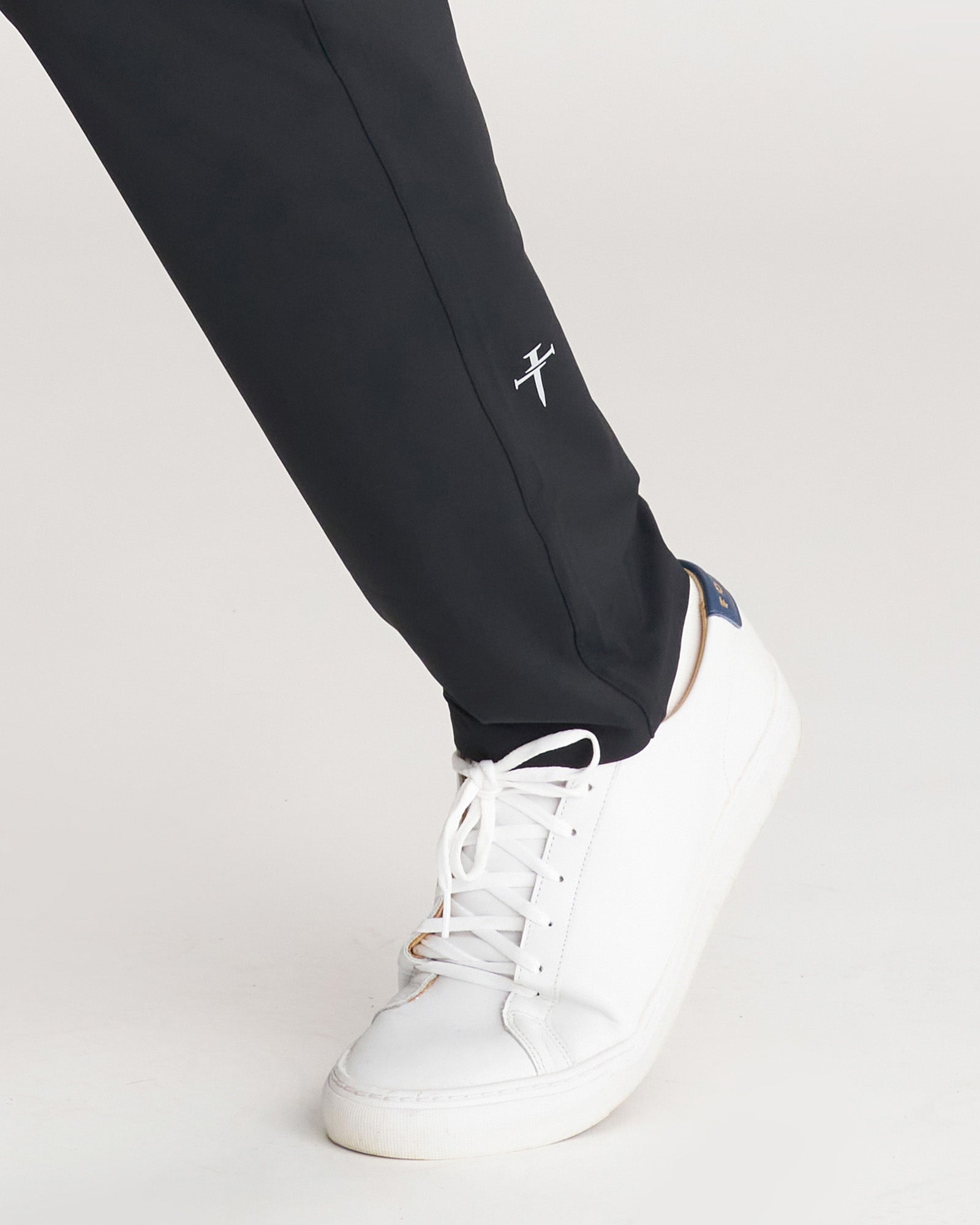 Close-up of black Links Golf Pant ankle and hem with white logo, paired with white leather sneakers.