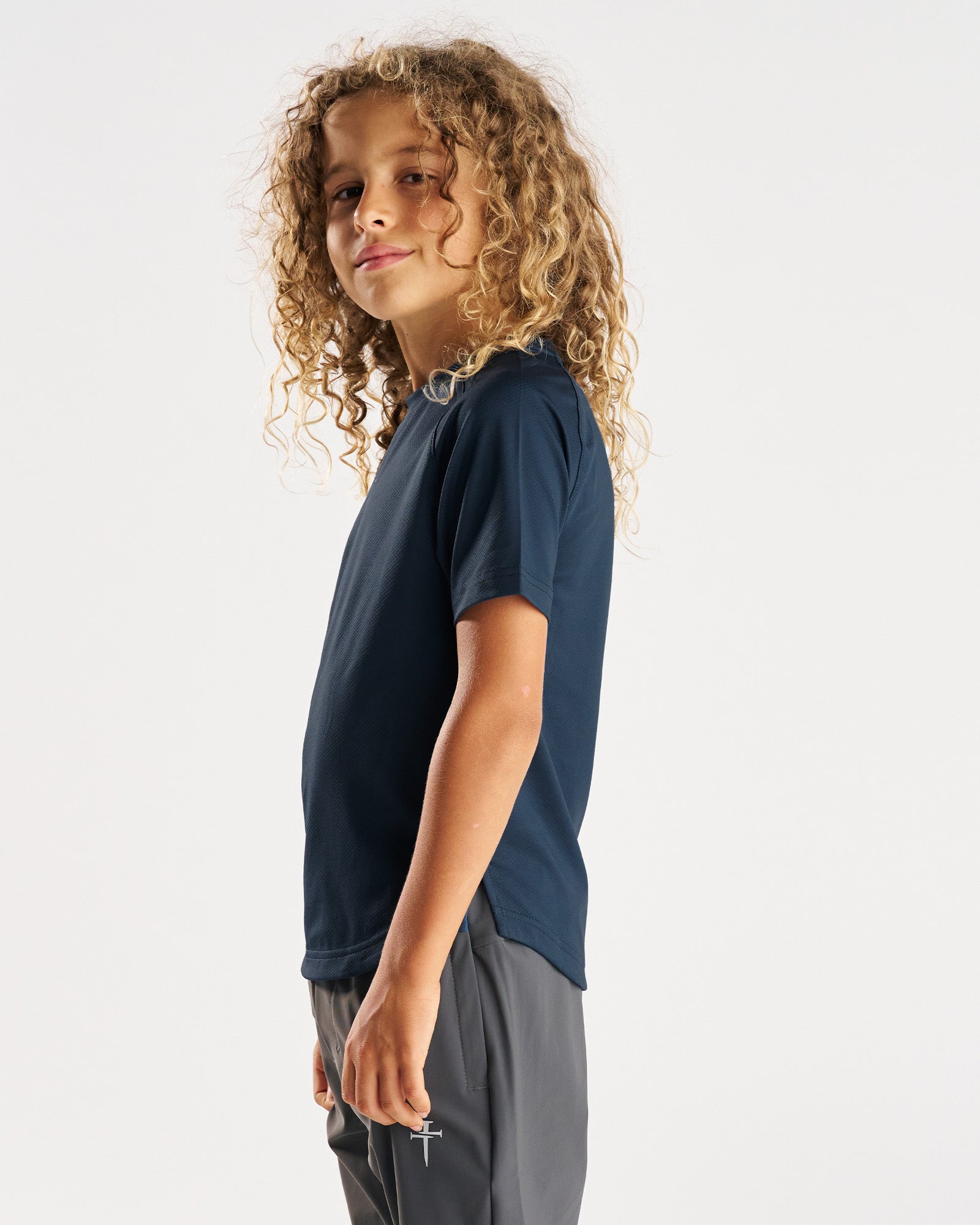 Youth Pro-Tech Tee Cross in Midnight Navy on a child model shown from a side angle.