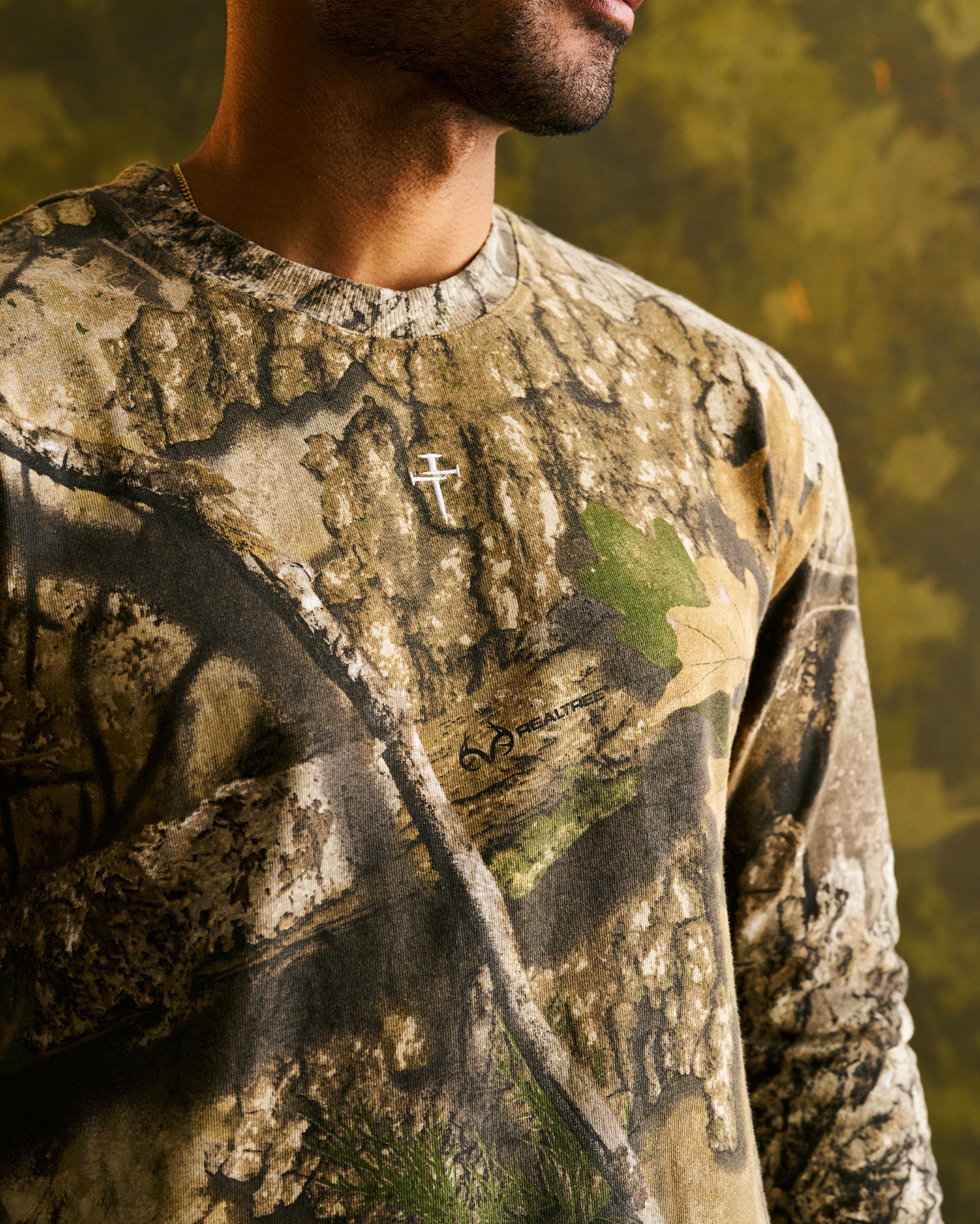 Close-up of FHG Realtree Camo long sleeve showing Realtree logo and cross embroidery detail on chest.