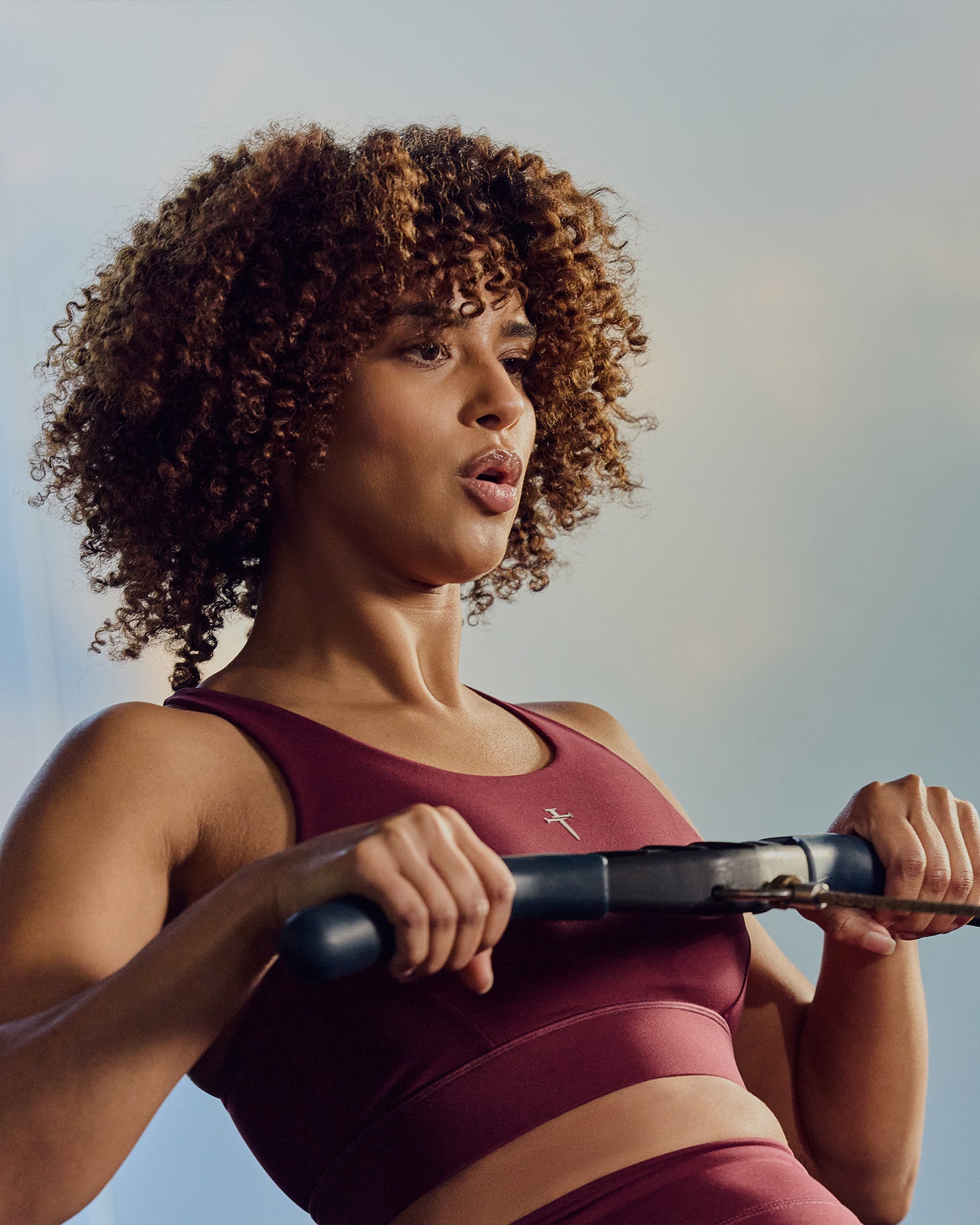 Model wearing Merlot Crossback Sports Bra, upper body close-up, slight side angle, holding exercise equipment.