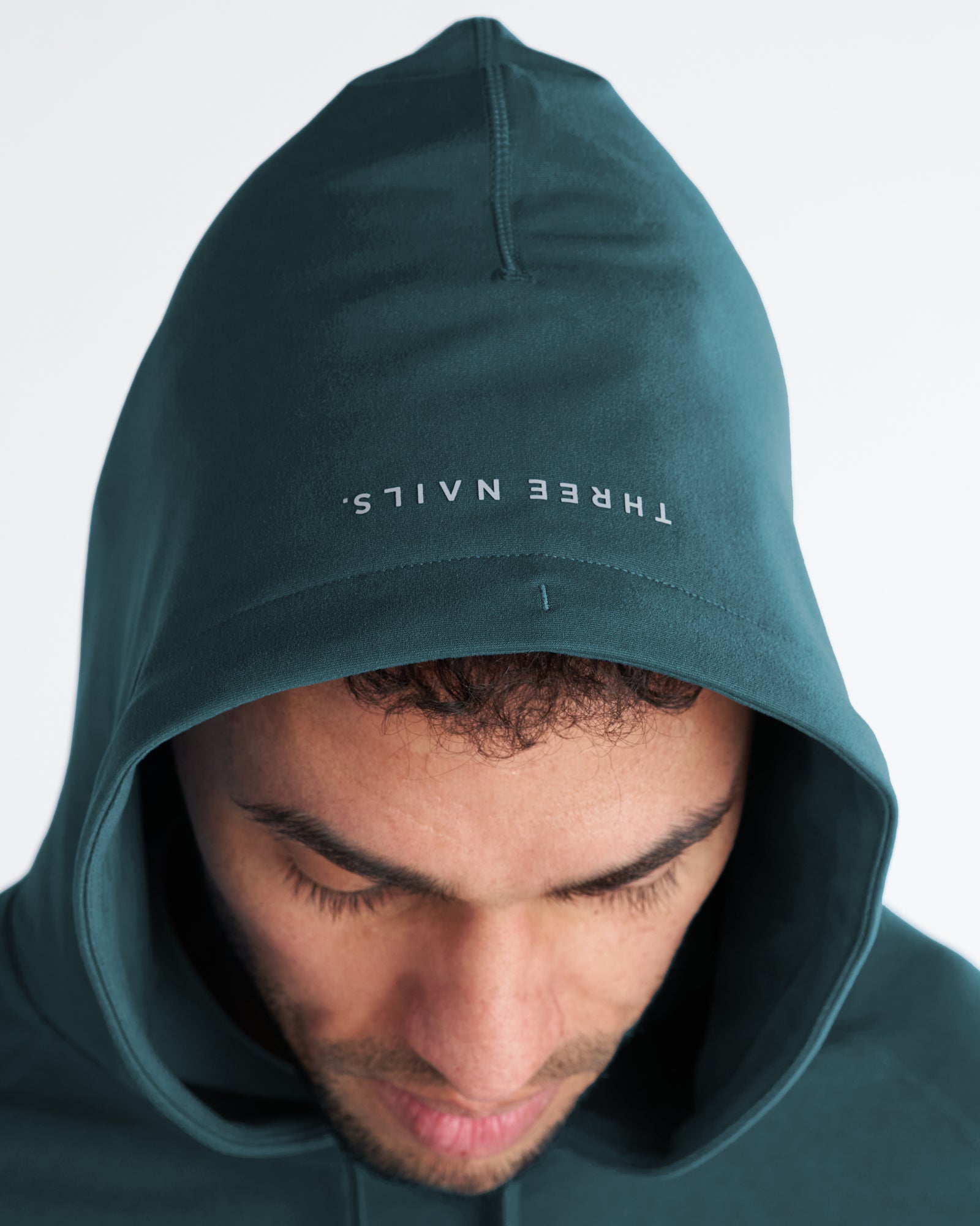 Close-up of model wearing the Haven Performance Hoodie in Teal, showing hood detail with mirrored Three Nails branding.