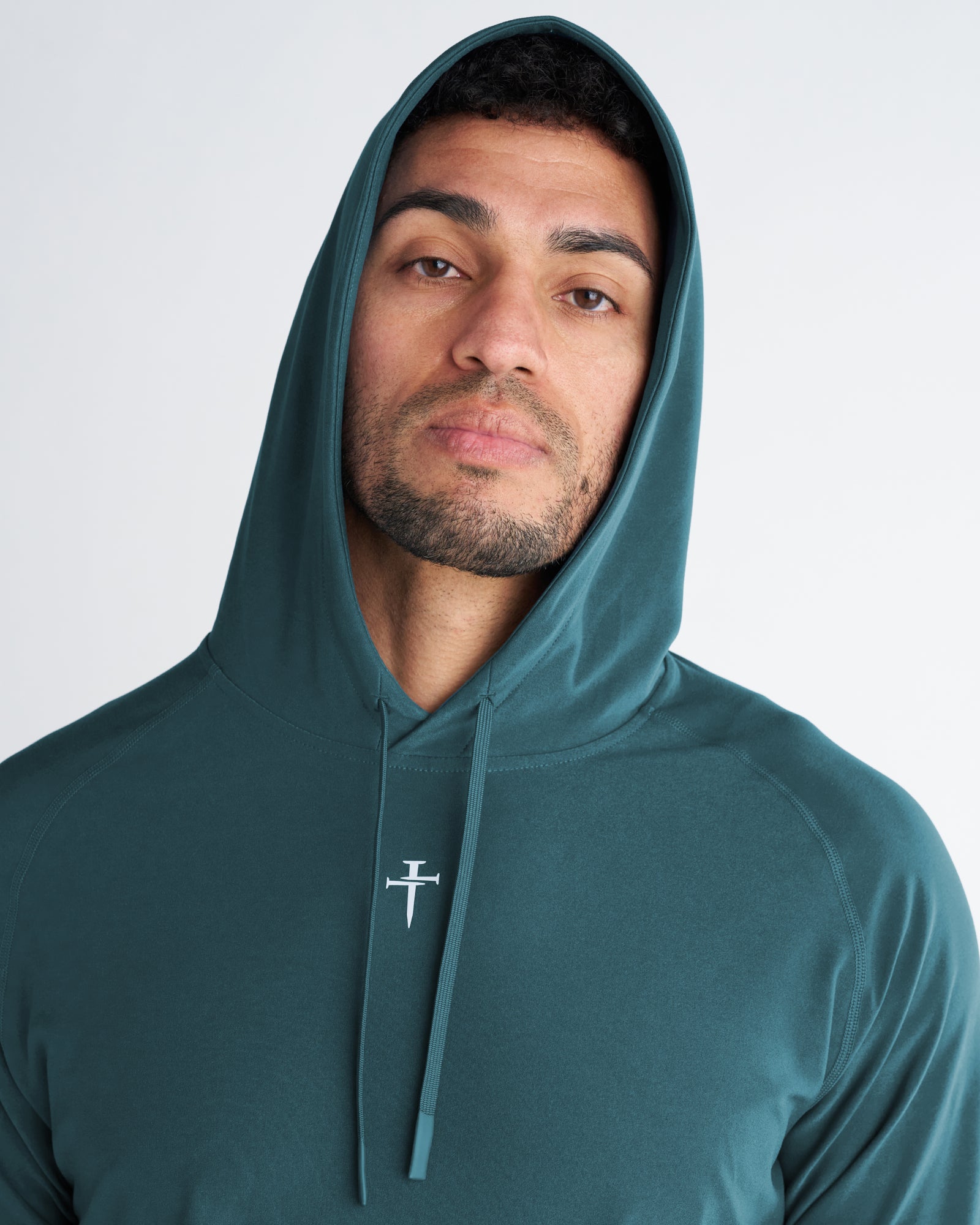 Close-up front view of Haven Performance Hoodie in teal worn by male model, showing hood up and cross logo detail.