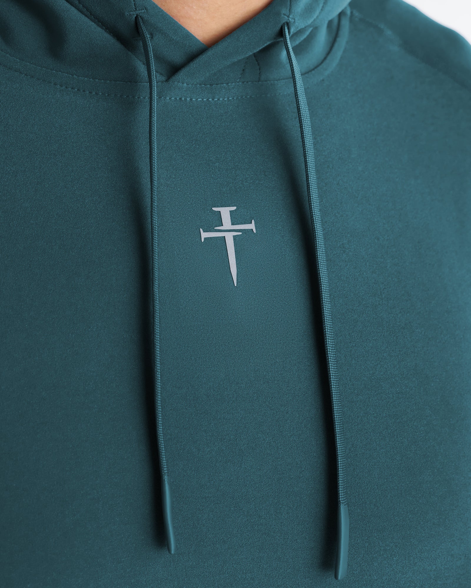 Haven Performance Hoodie in teal, close-up detail shot of the nail cross logo on the chest with drawstring cords visible.