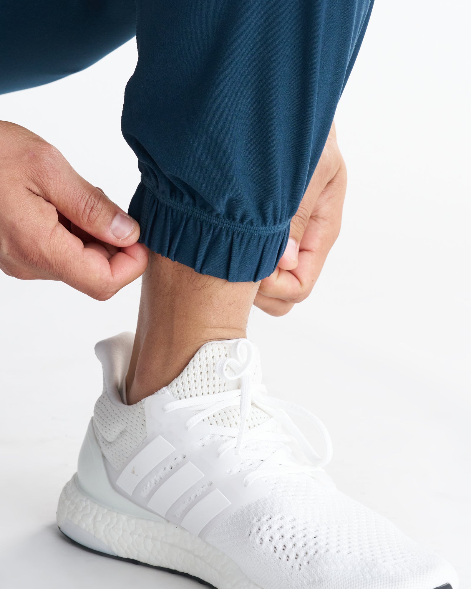 Close-up of the Haven Performance Jogger in Midnight Navy showing the elastic ribbed ankle cuff on a model wearing white Adidas sneakers.