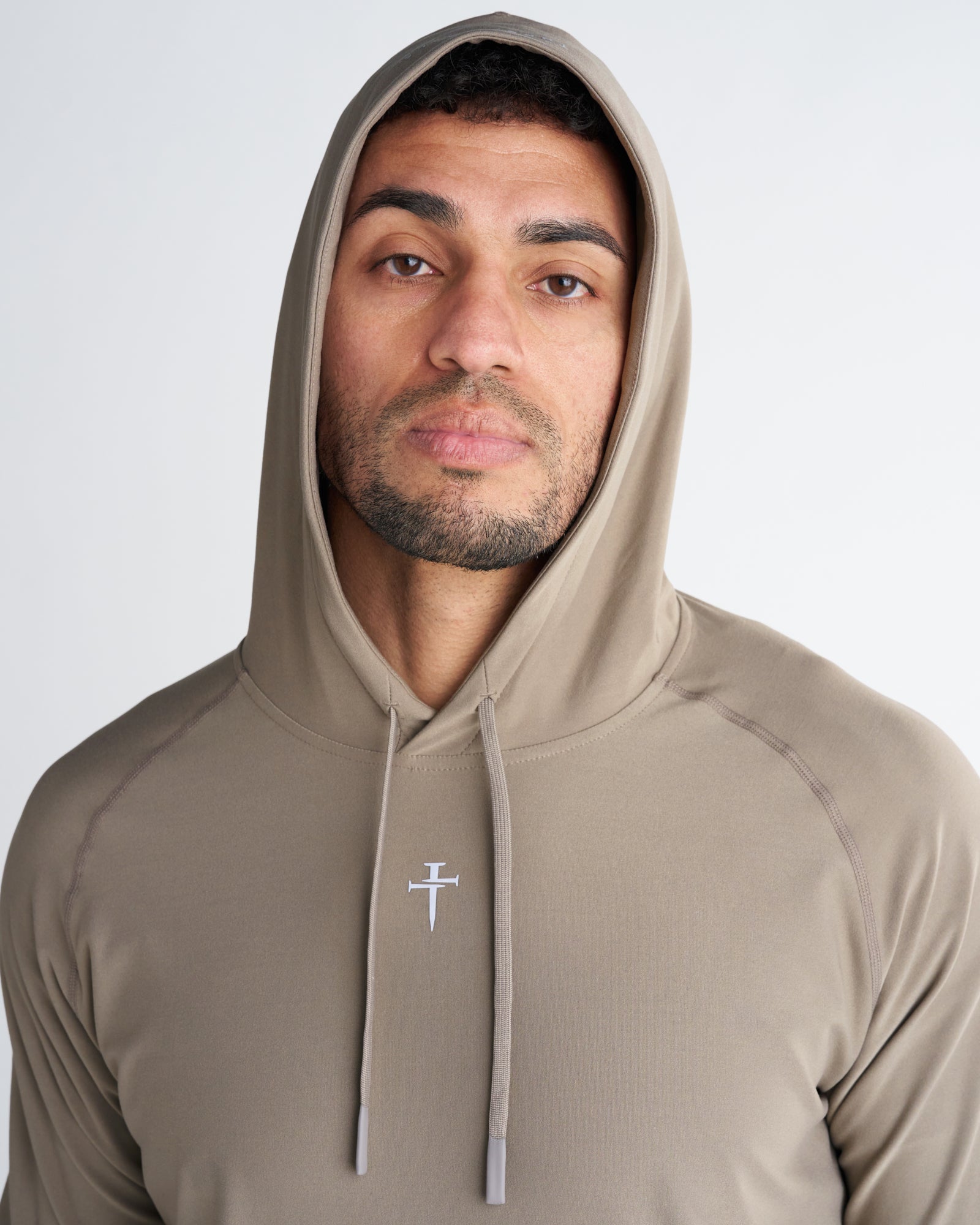 Haven Performance Hoodie in Sand, close-up front view on male model showing hood up and embroidered nail cross logo.
