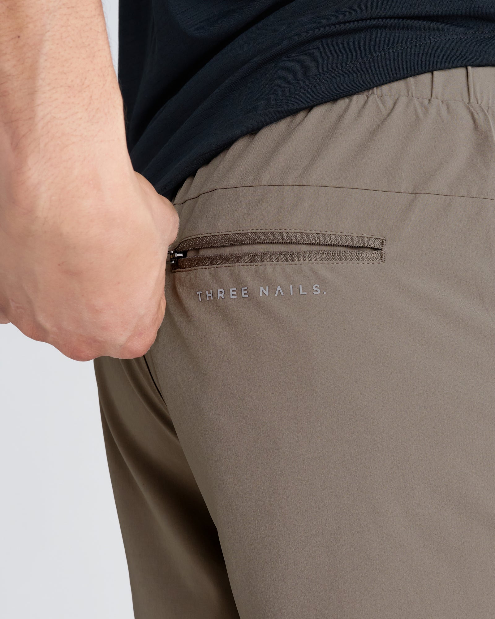 Close-up of Pulse Tech Liner Short in Sand showing back zip pocket with Three Nails branding.