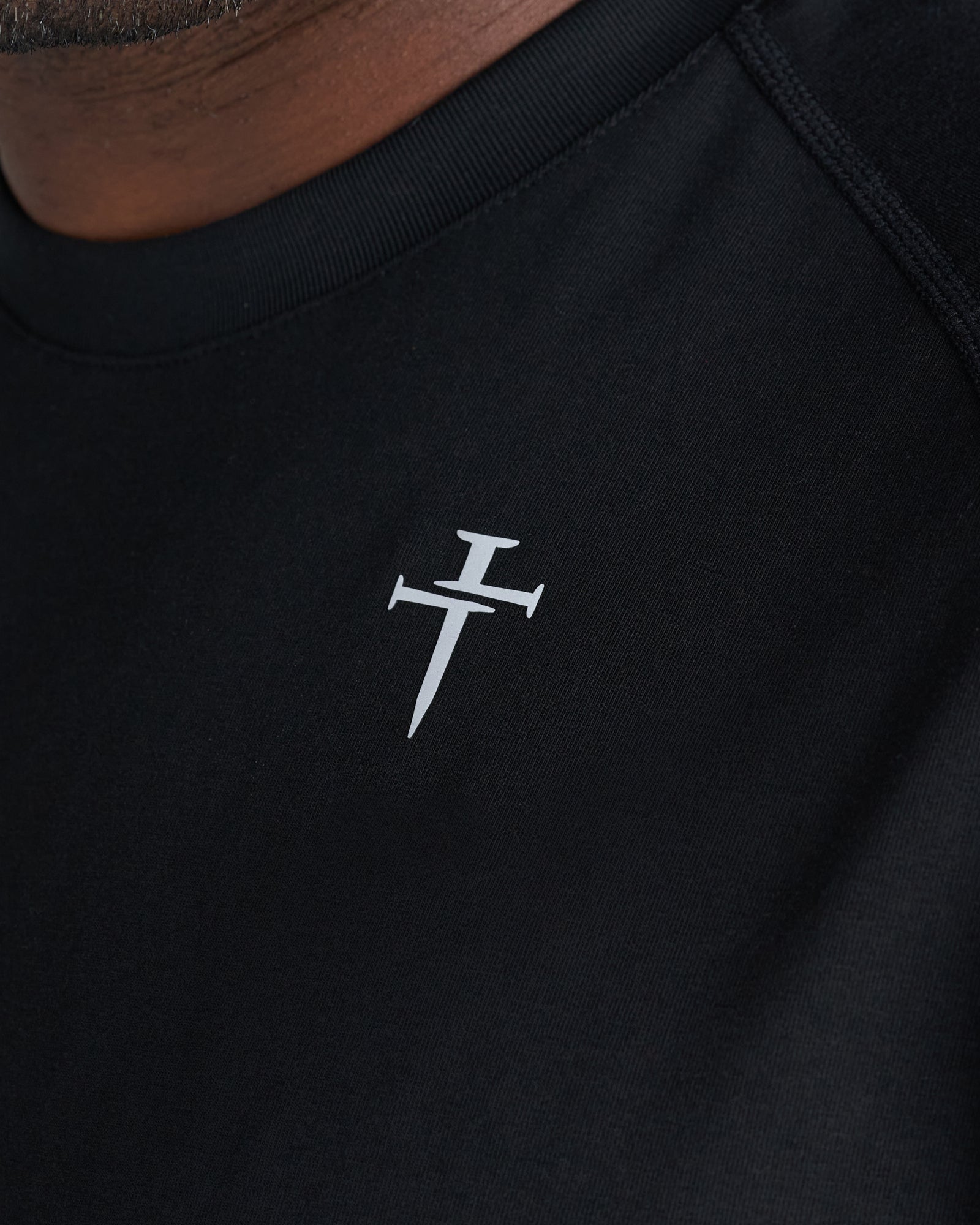 Close-up of the Core Tee in black showing a small three nails cross logo on the chest.