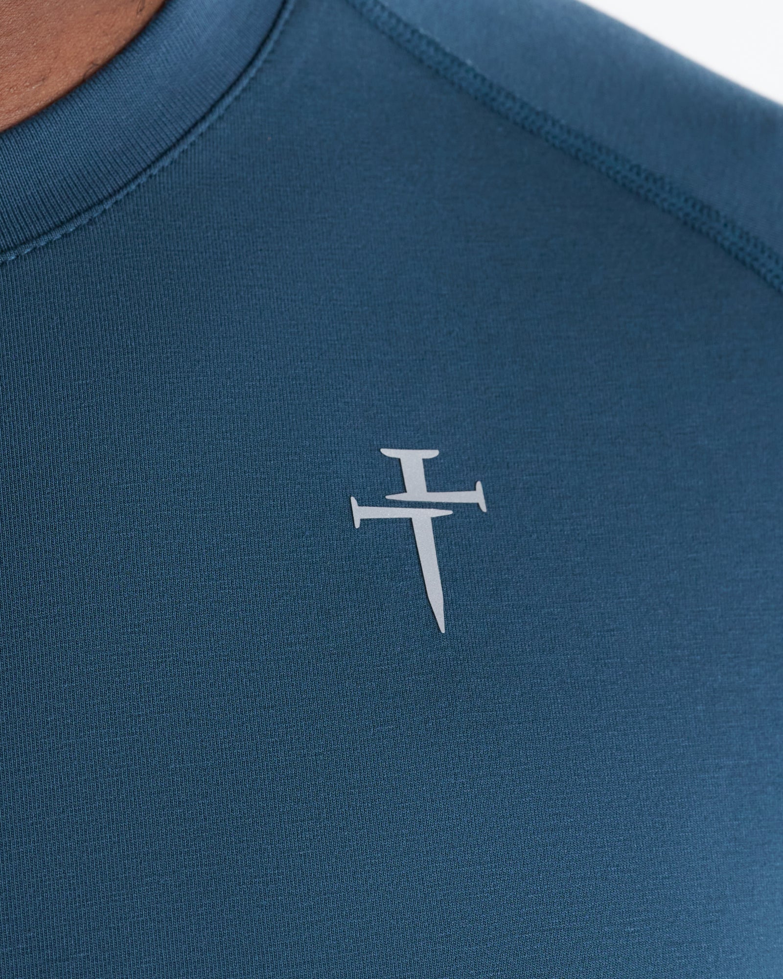 Close-up detail of the Core Tee in Midnight Navy showing the Three Nails cross logo on the chest.
