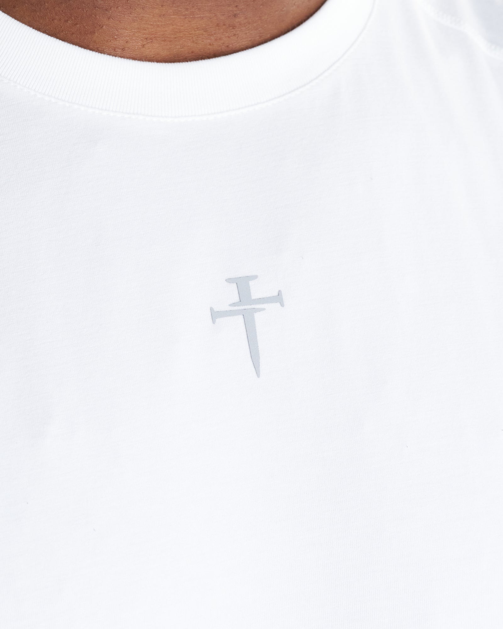 Close-up of the Core Raglan Cutoff White chest area showing a small gray nail cross logo.