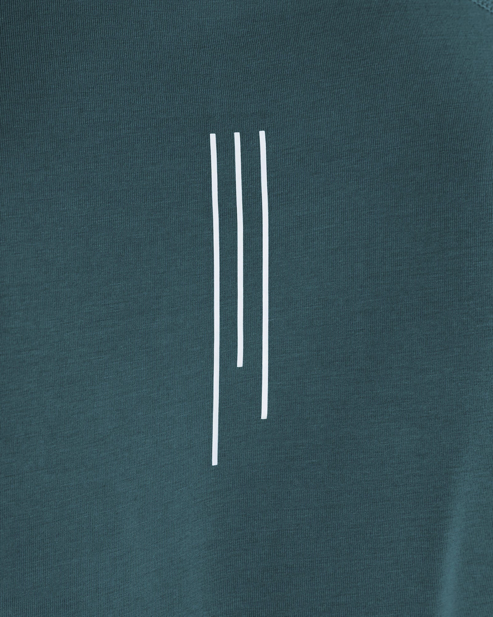 Close-up detail of the Core Raglan Cutoff in teal showing three white vertical lines printed on the chest.