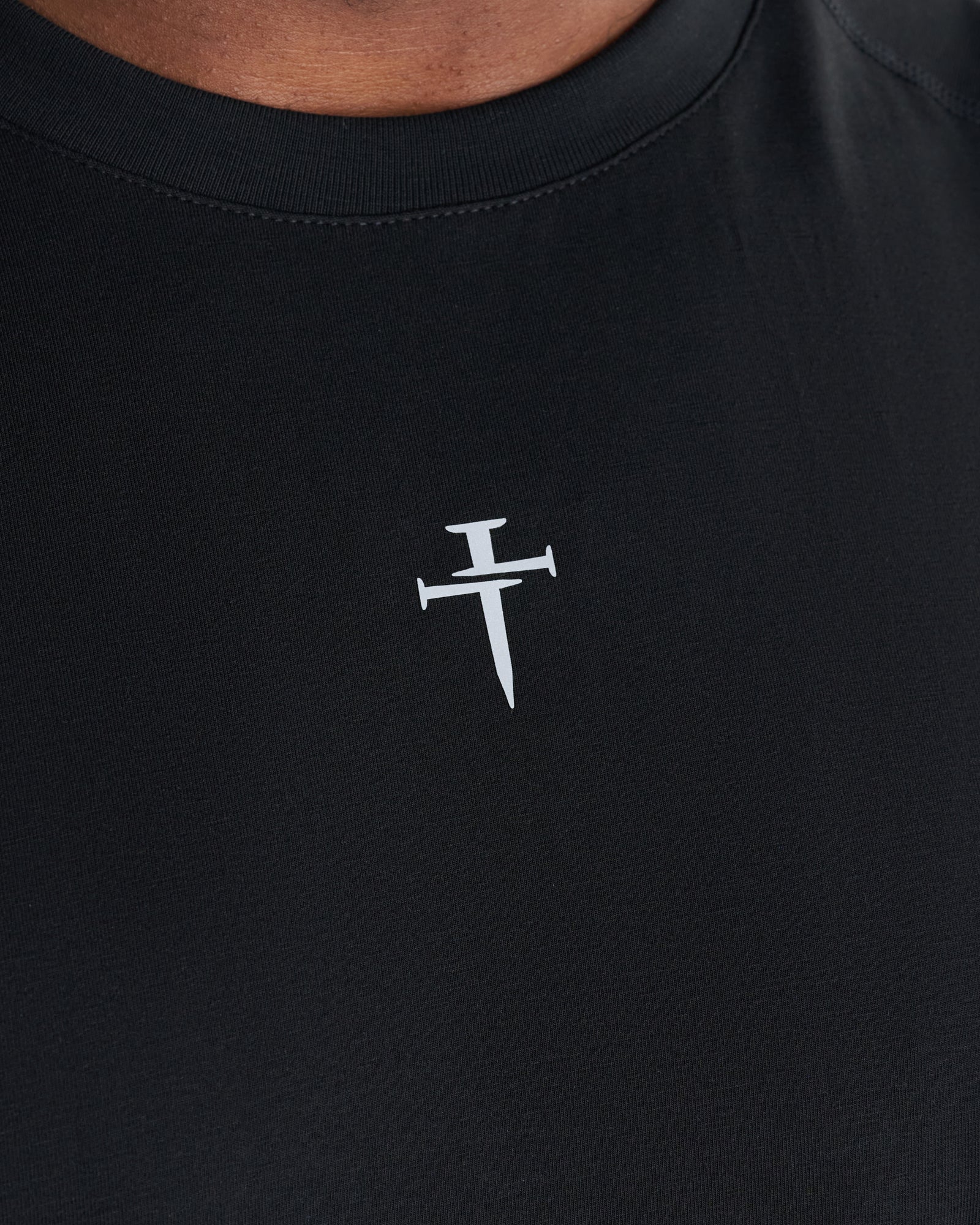 Close-up of the Core Raglan Cutoff in black showing a small white nails cross logo on the chest.