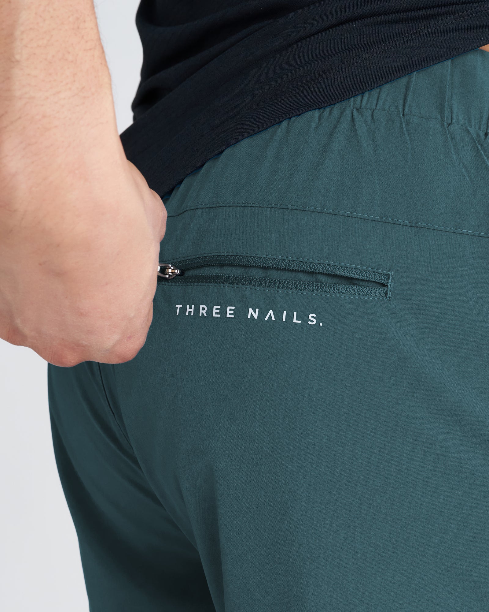 Close-up of the Pulse Tech Liner Short in Teal showing the zippered back pocket with Three Nails branding.