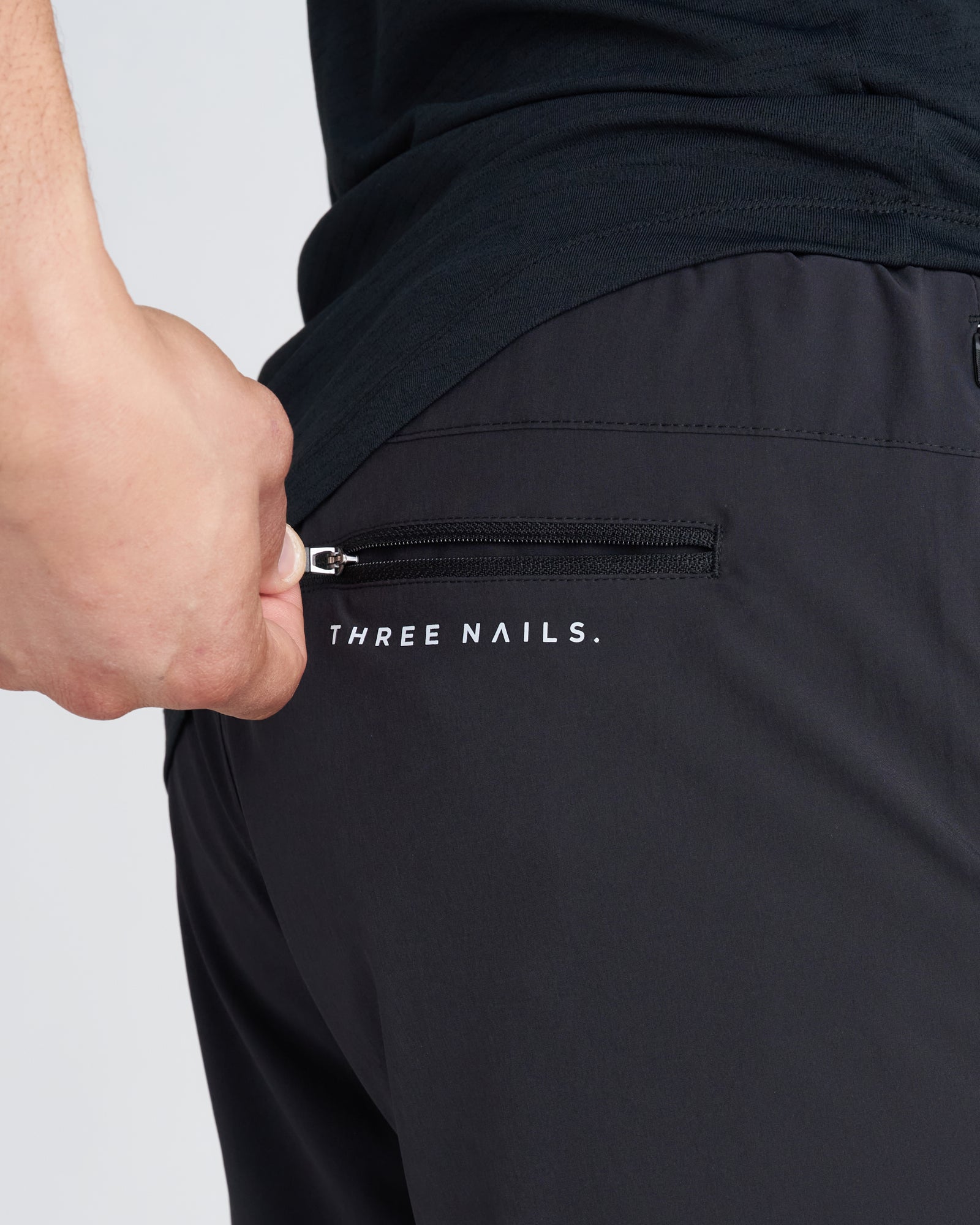 Close-up of black Pulse Tech Liner Short back zip pocket with Three Nails branding.