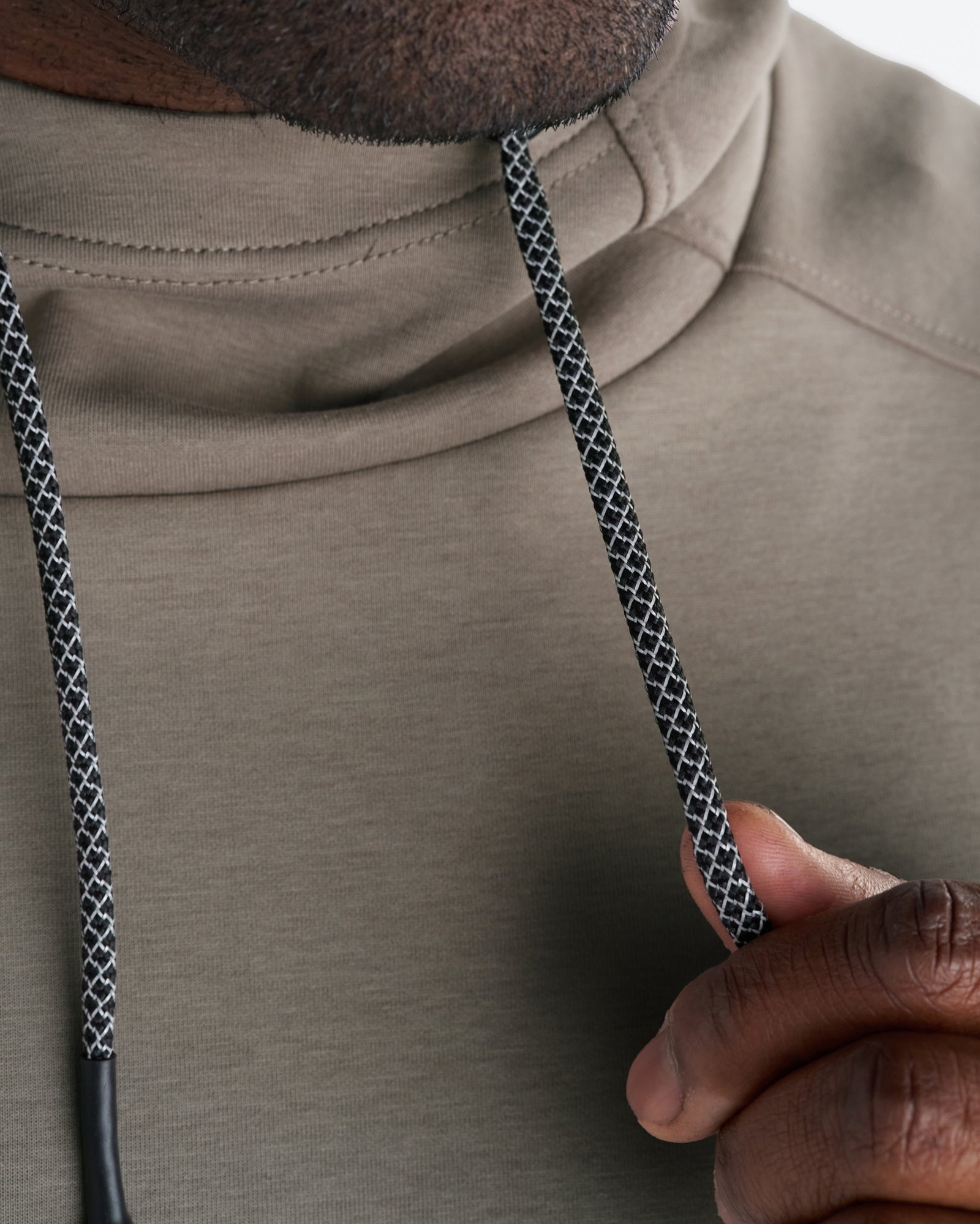 Close-up detail of the Pro-Tech Hoodie in Sand showing black and white woven drawstrings held by a models hand.