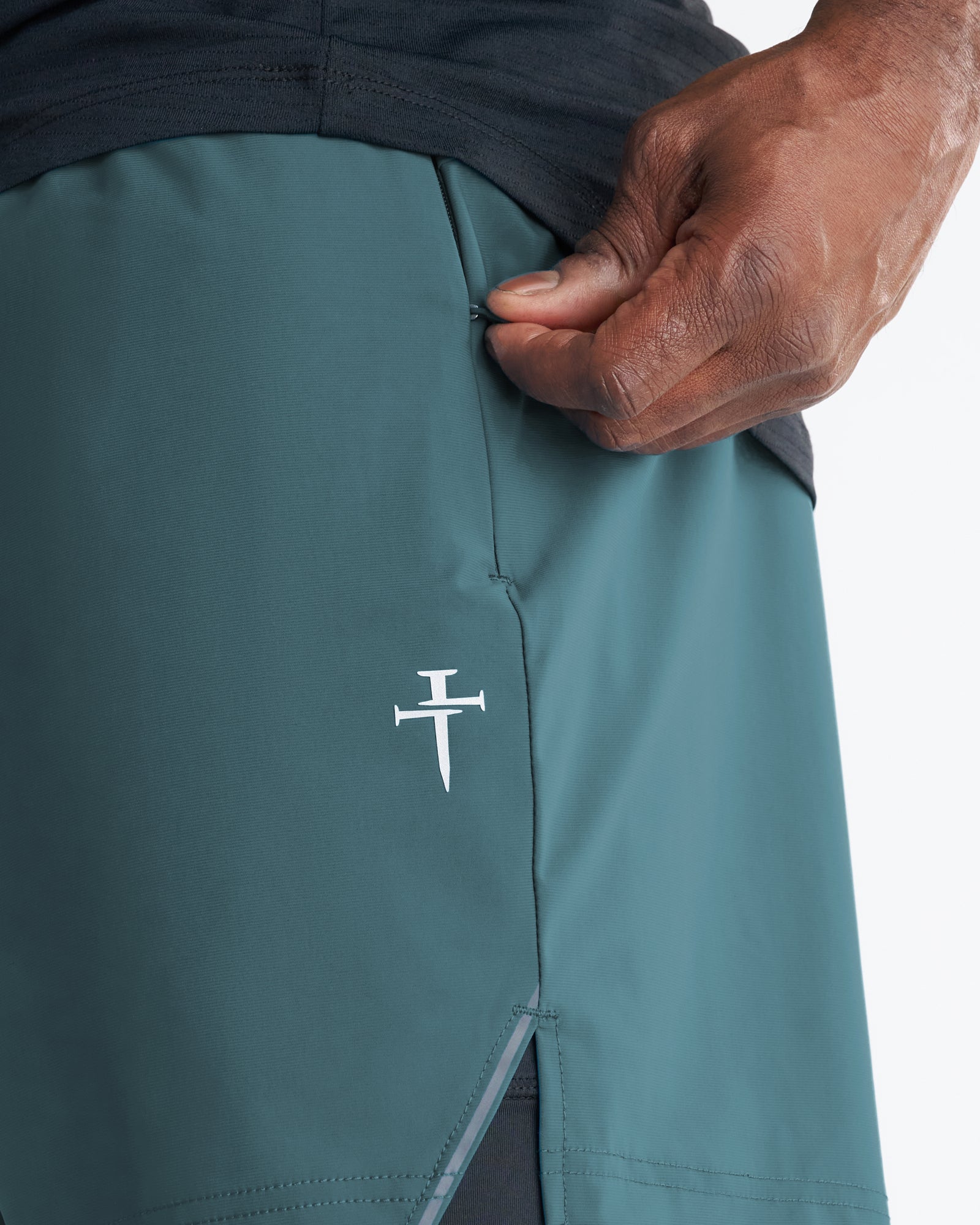 Close-up detail of Vapor-Lite Liner 5-inch Short in teal showing side zip pocket and embroidered cross logo.