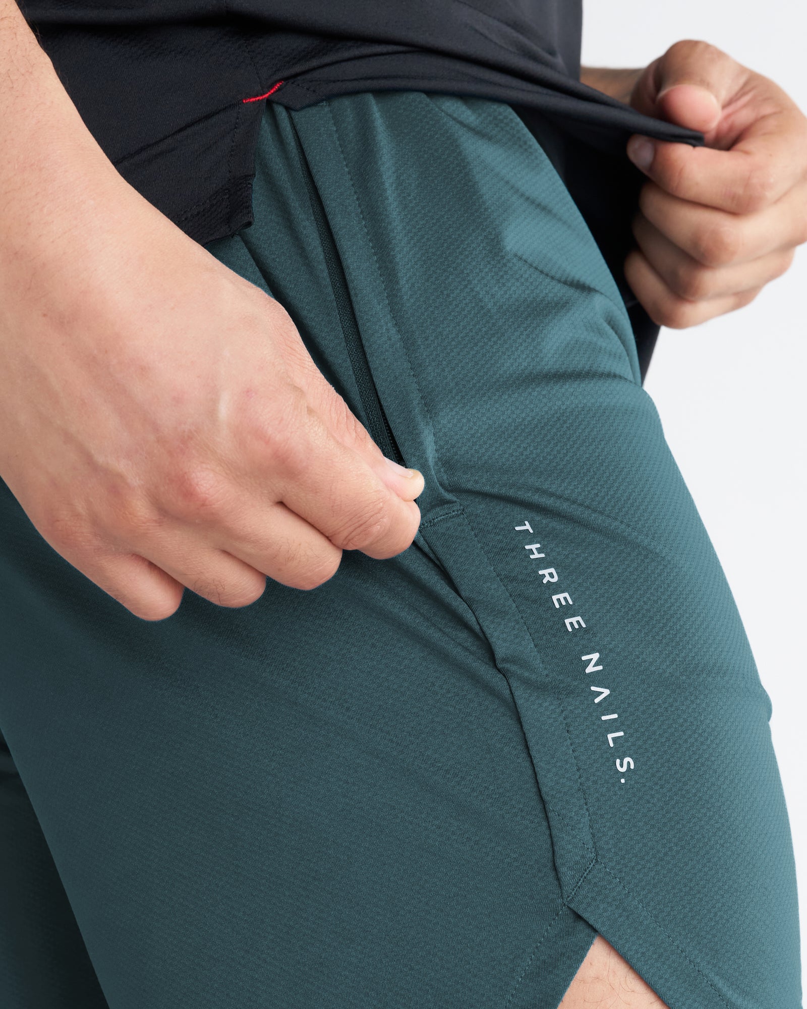 Close-up of the Pro-Tech 2.0 Linerless Short in Teal showing the side pocket opening and Three Nails branding.