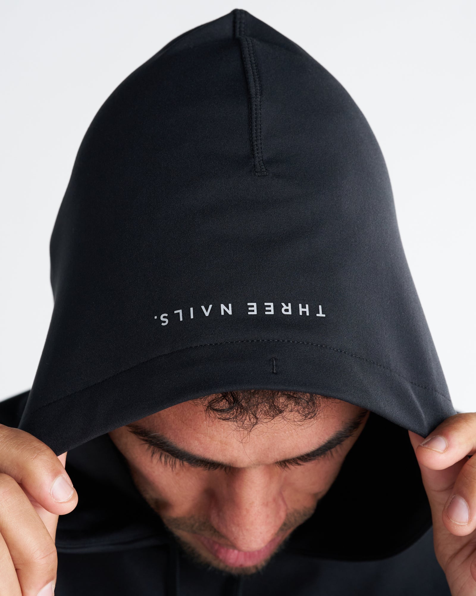 Close-up of the Haven Performance Hoodie in black showing the interior hood brim with mirrored Three Nails logo print.