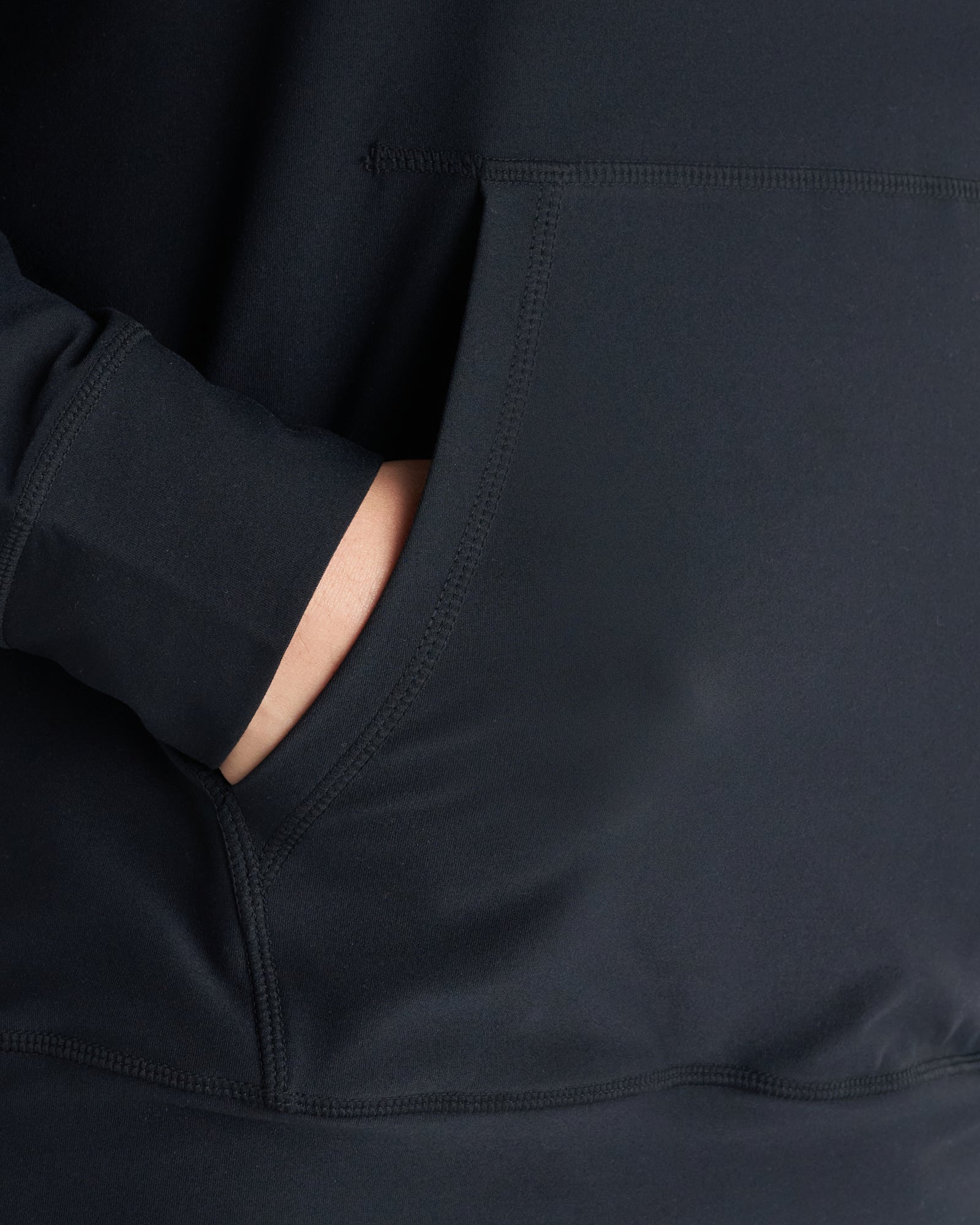 Haven Performance Hoodie in black, close-up detail of hand tucked into side pocket showing stitching and fabric texture.