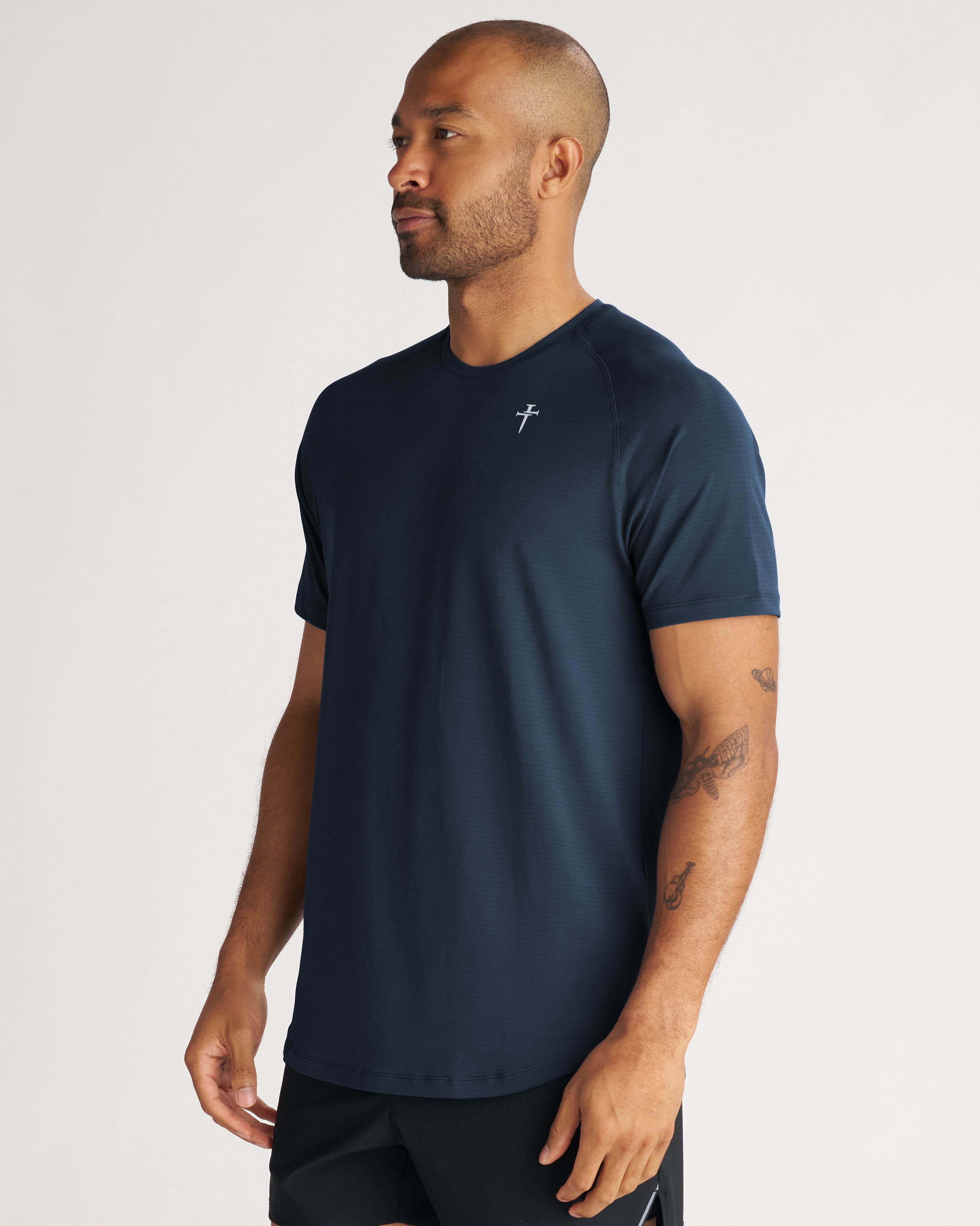 Aion-Lite Tee Cross in Midnight Navy on a male model at a slight side angle, showing raglan sleeves and small cross logo.
