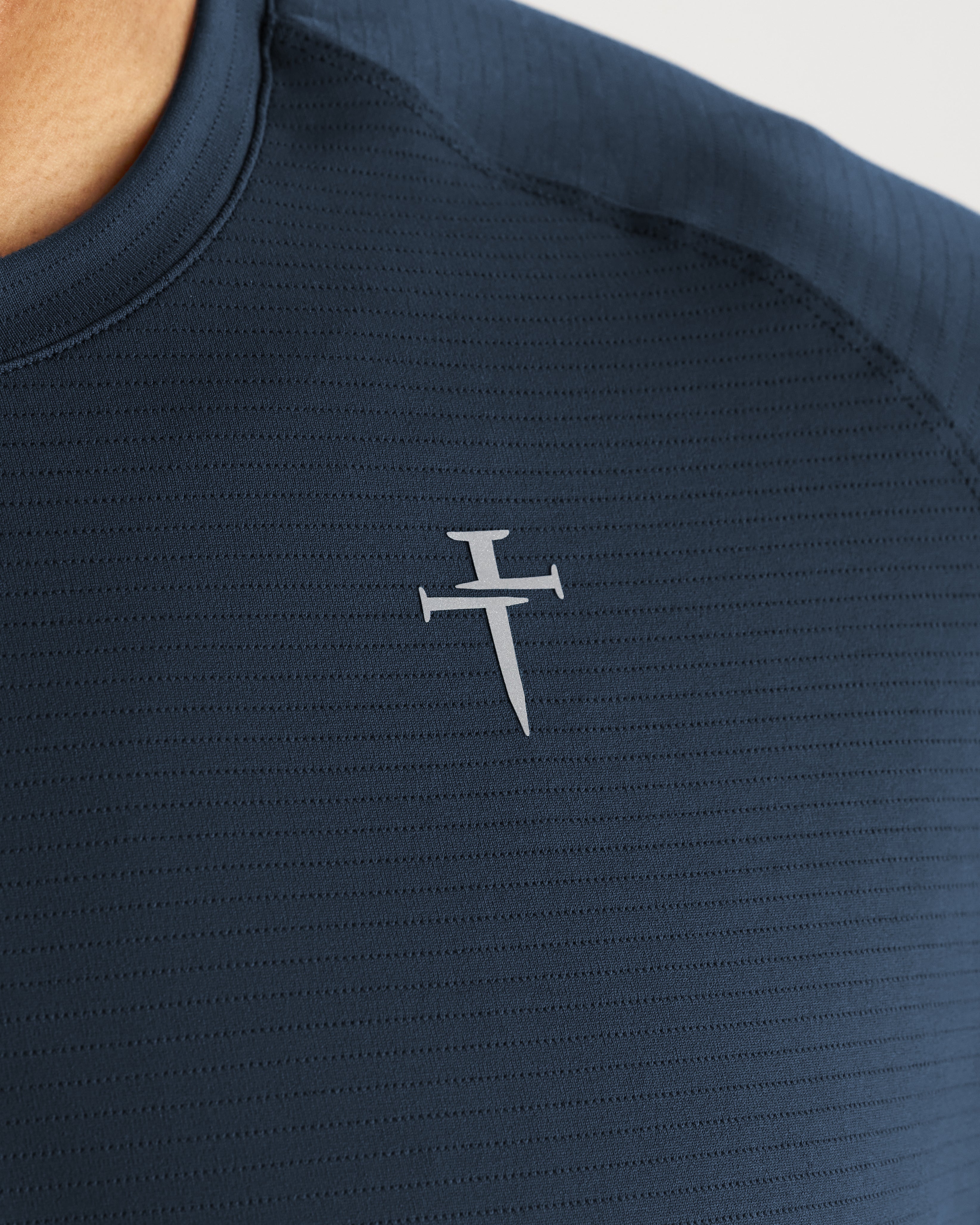 Close-up of Aion-Lite Tee Cross in Midnight Navy showing ribbed fabric texture and small cross logo on chest.