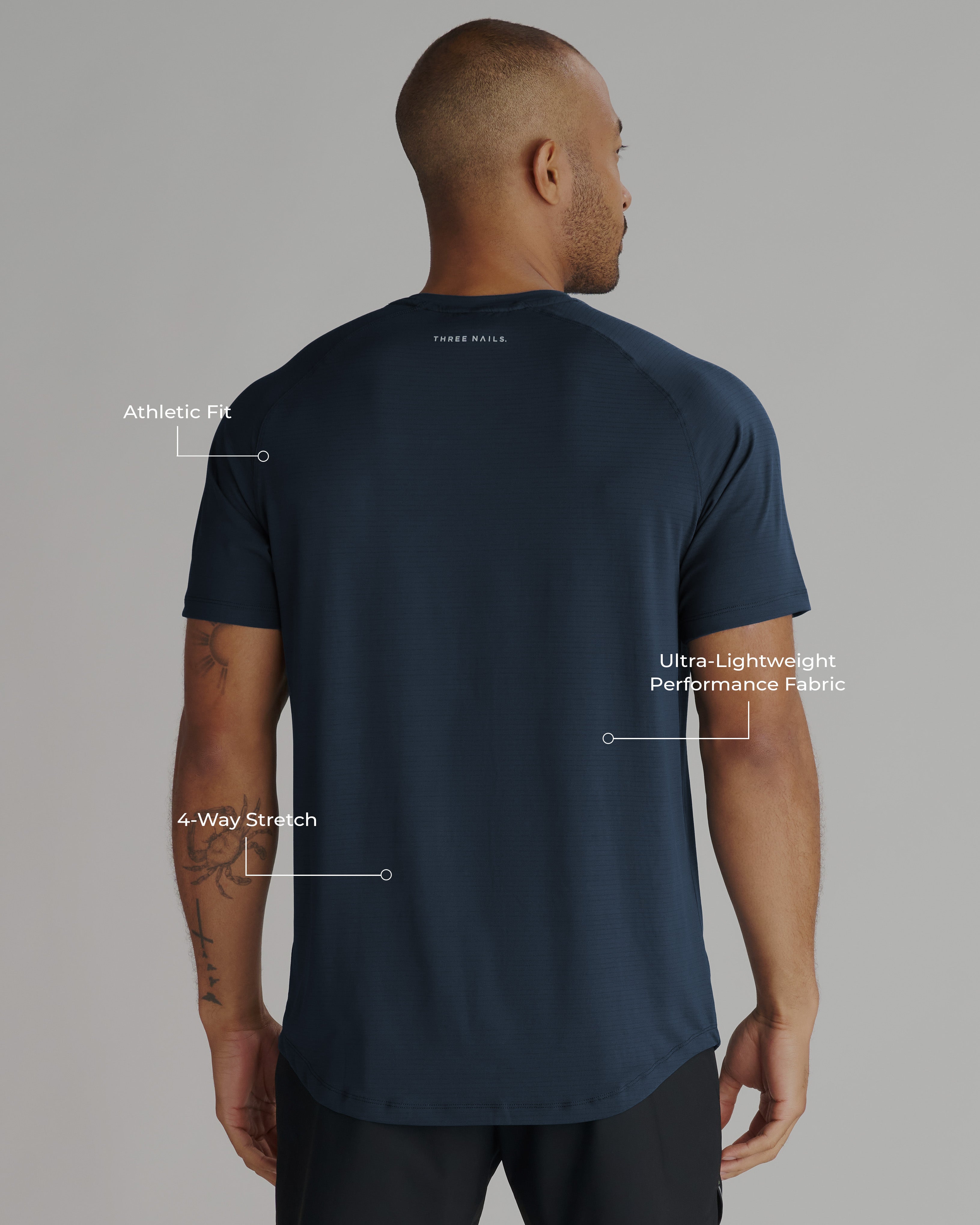 Back view of a man wearing the Aion-Lite Tee in Midnight Navy with feature callouts highlighting fit and fabric.