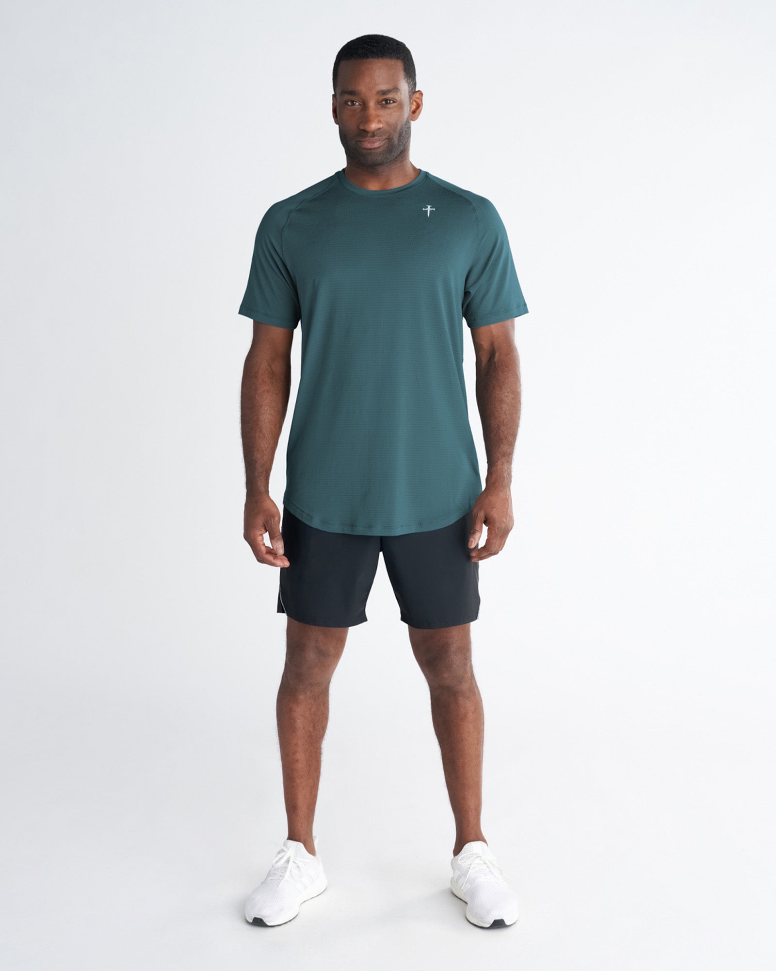 Man wearing the Core Tee in Teal, front view, paired with black shorts and white sneakers.