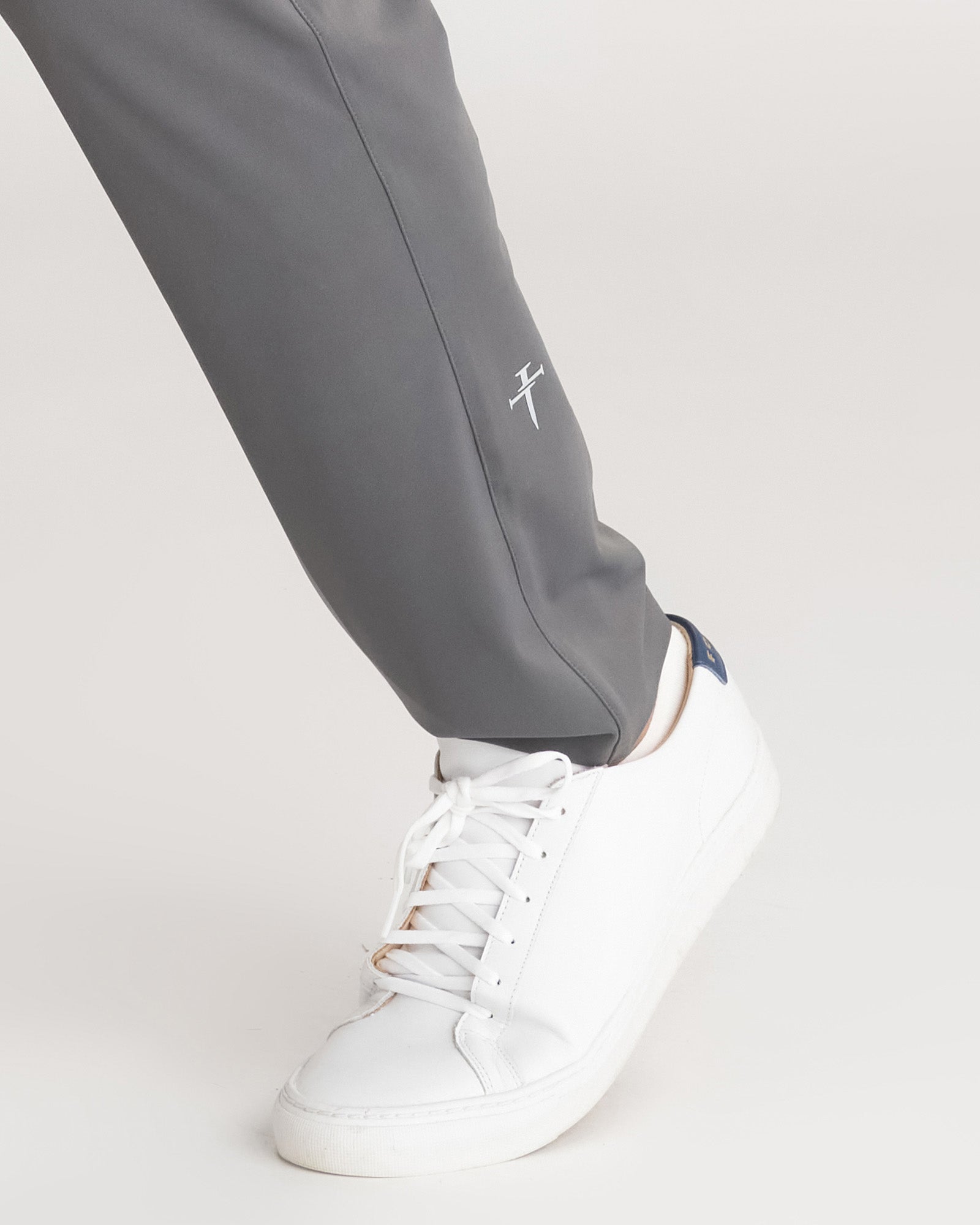 Close-up of Links Golf Pant in Space Grey showing the tapered ankle hem and small cross logo above a white sneaker.