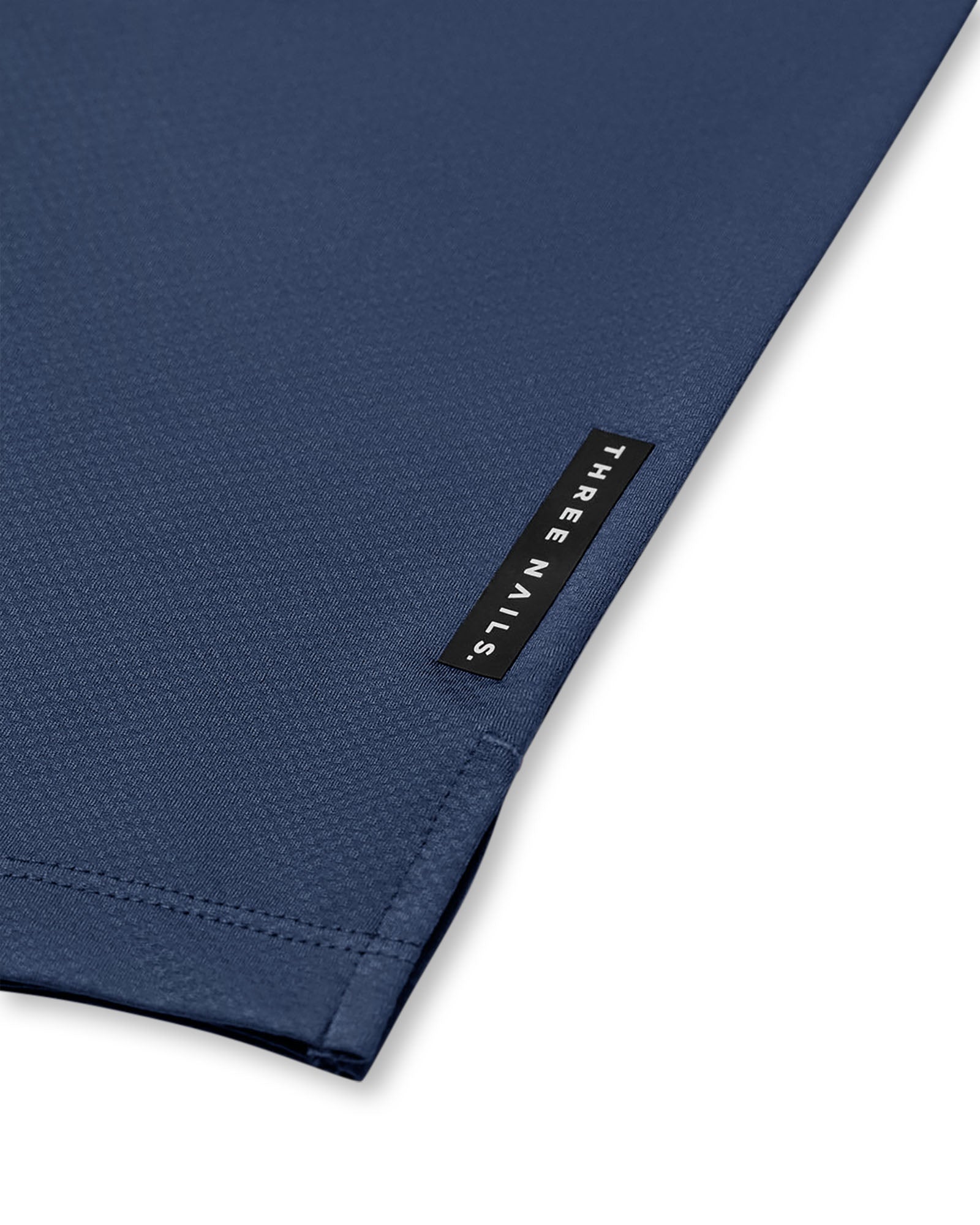 Close-up detail of the Pro-Tech Tee Midnight Navy hem, showing fabric texture and Three Nails woven label tag.