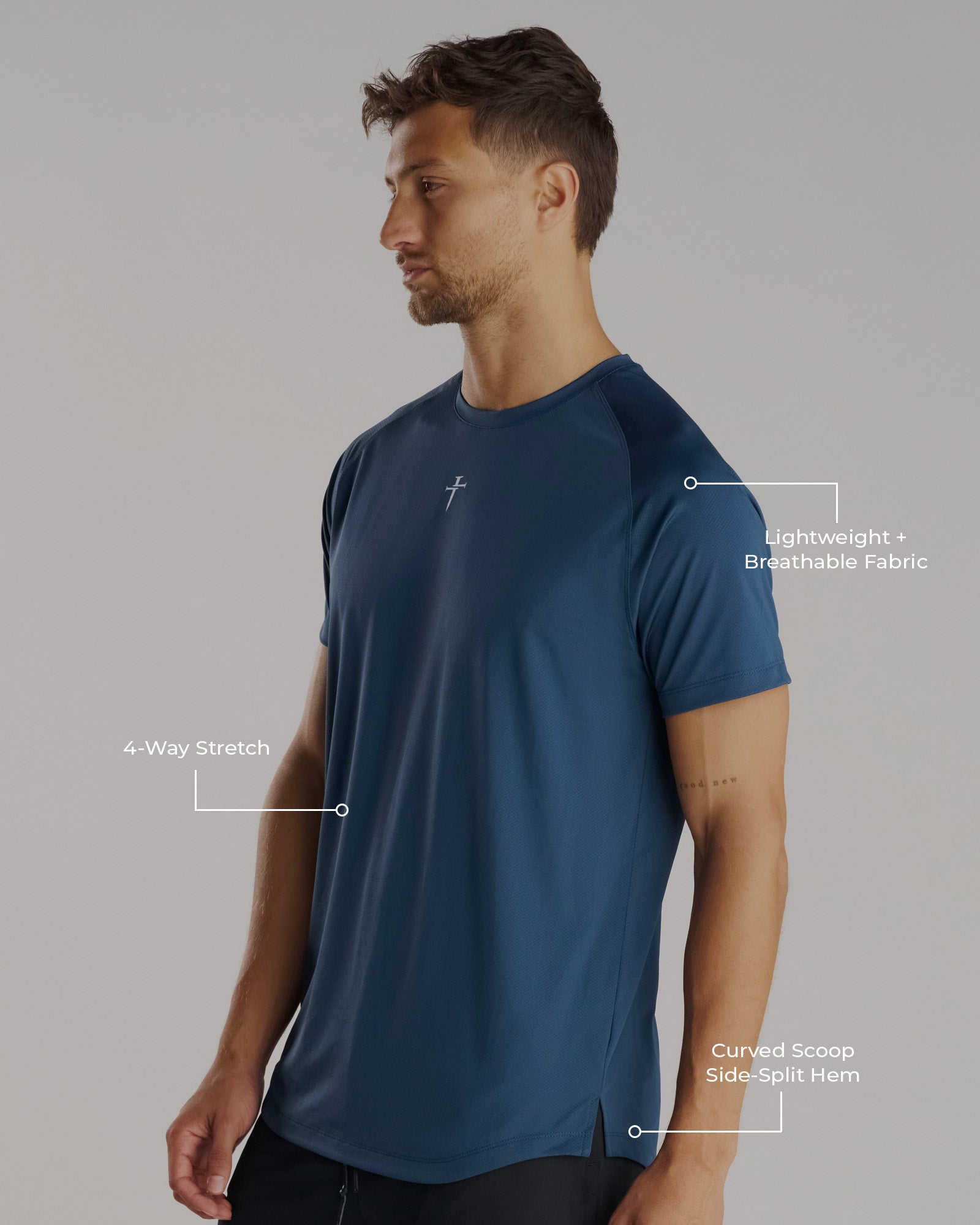 Man modeling the Pro-Tech Tee Cross in Midnight Navy, side angle, showing curved hem split and small cross logo.
