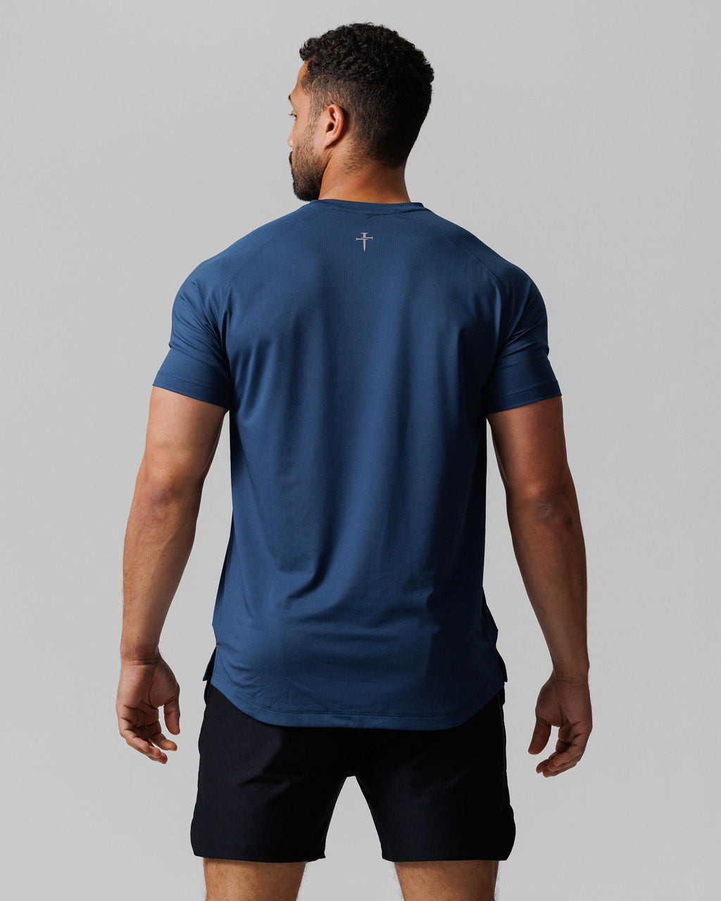 Back view of model wearing the Pro-Tech Tee Three Nails in Midnight Navy with black shorts.