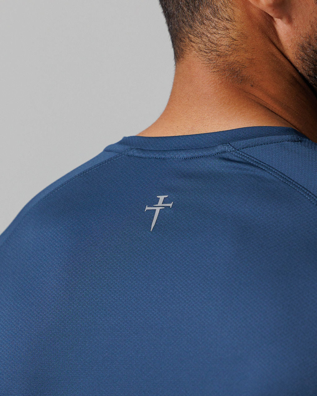 Close-up back detail of Pro-Tech Tee Three Nails in Midnight Navy showing the reflective logo near the collar.