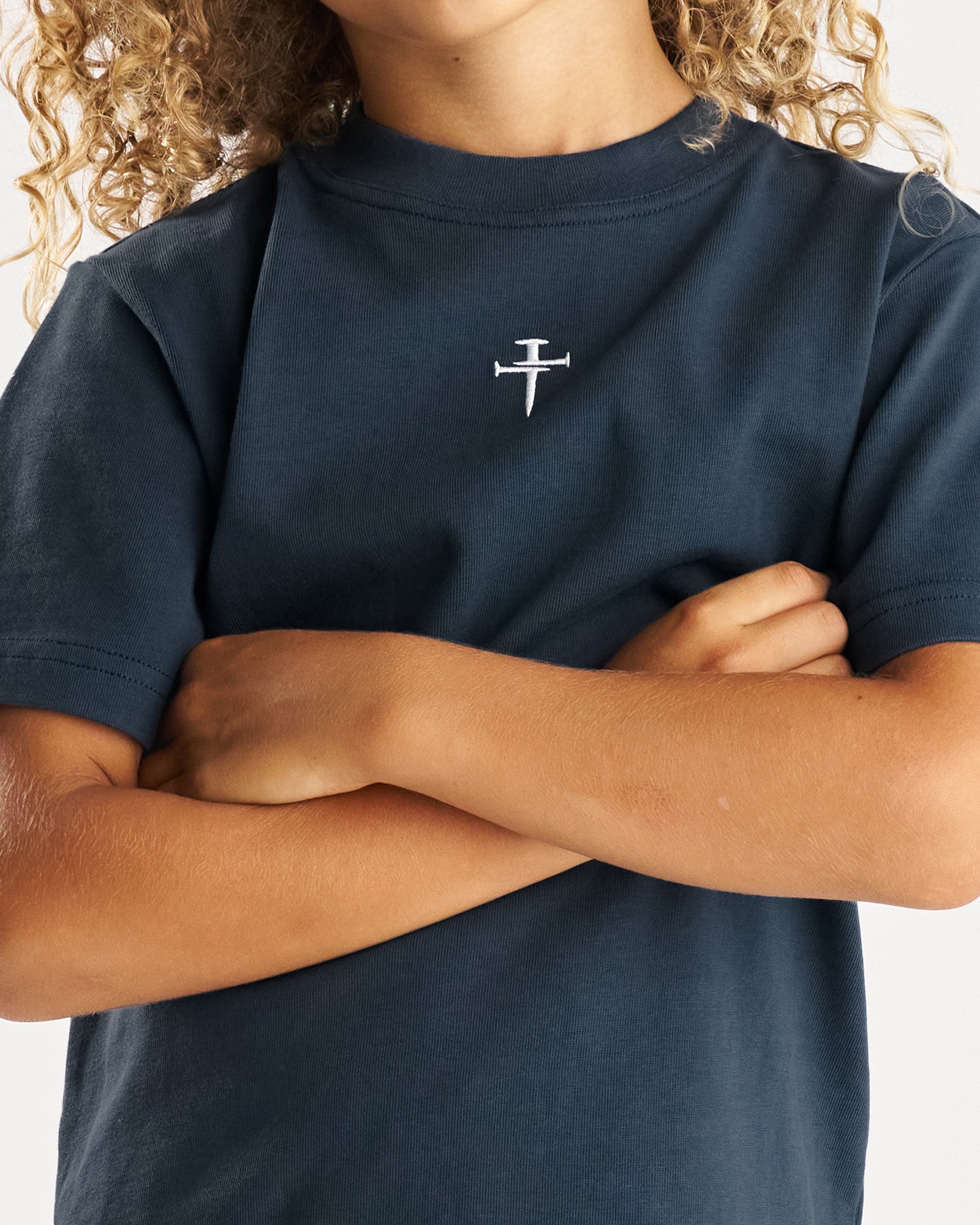 Close-up front view of Youth Heavyweight Cotton Oversized Tee FHG in Midnight Navy showing embroidered nail cross logo on chest.