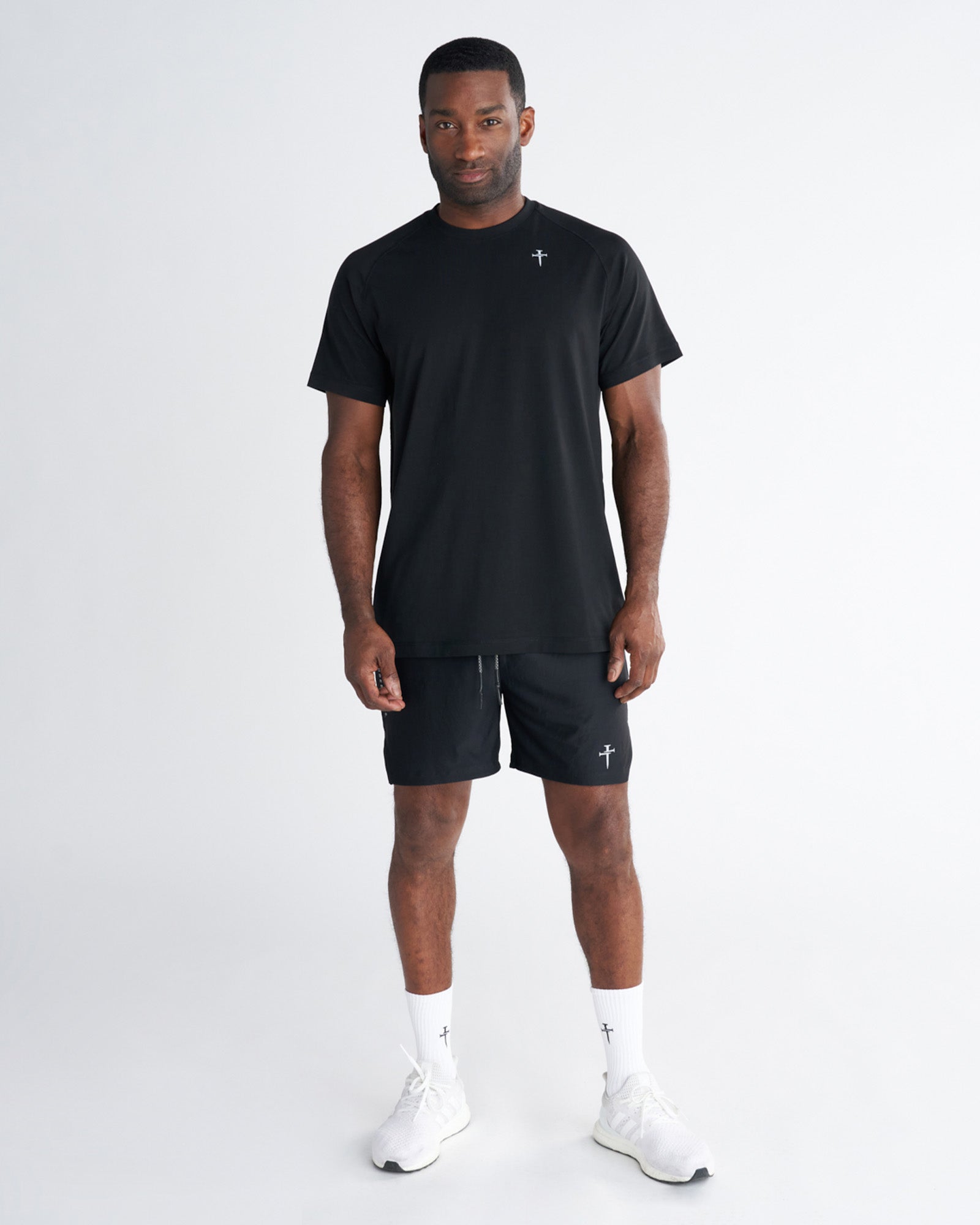 Man wearing black Core Tee, front view, paired with matching black shorts and white sneakers.