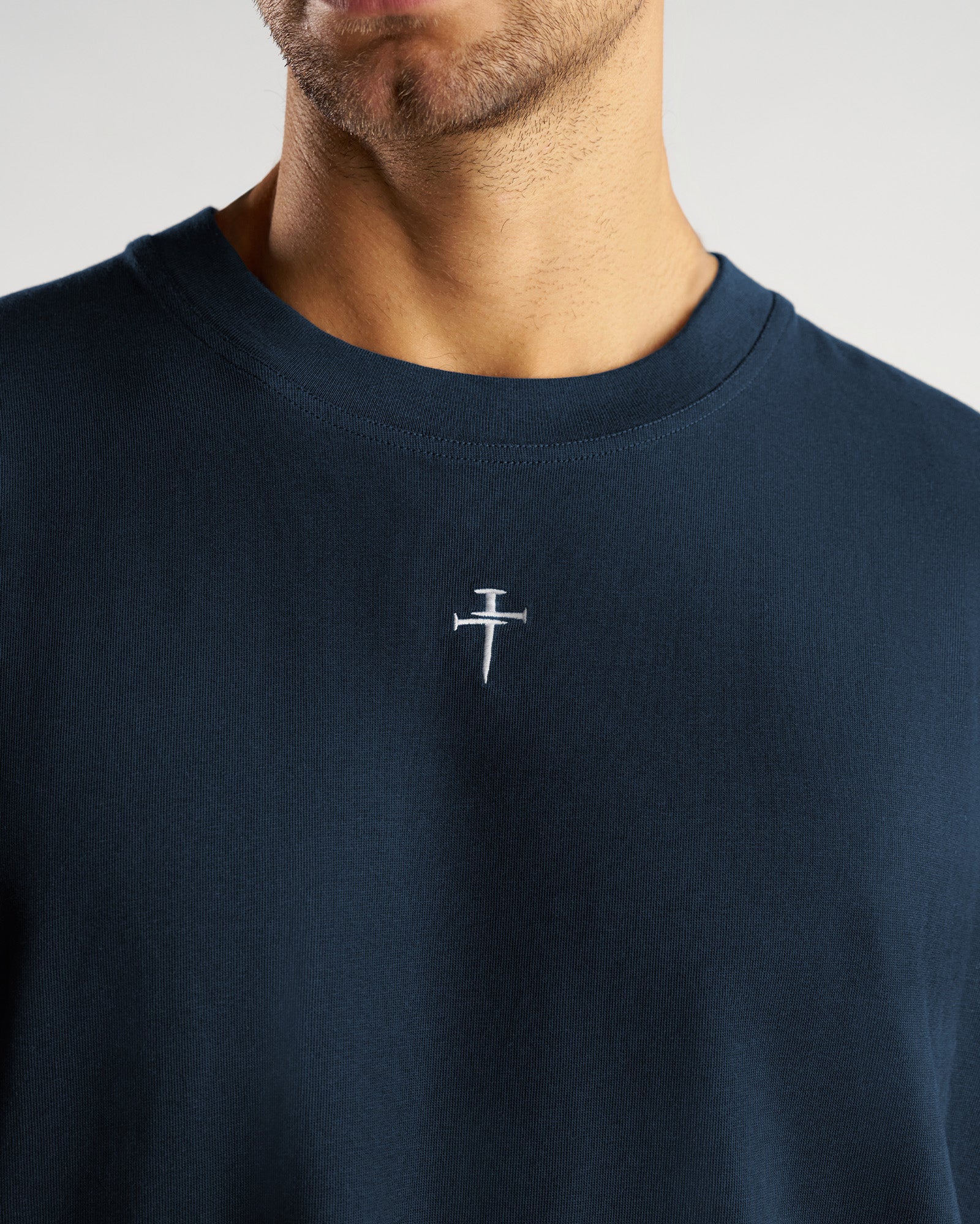 Close-up detail shot of the Heavyweight Cotton Oversized Long Sleeve FHG in Midnight Navy showing the embroidered nail cross logo.