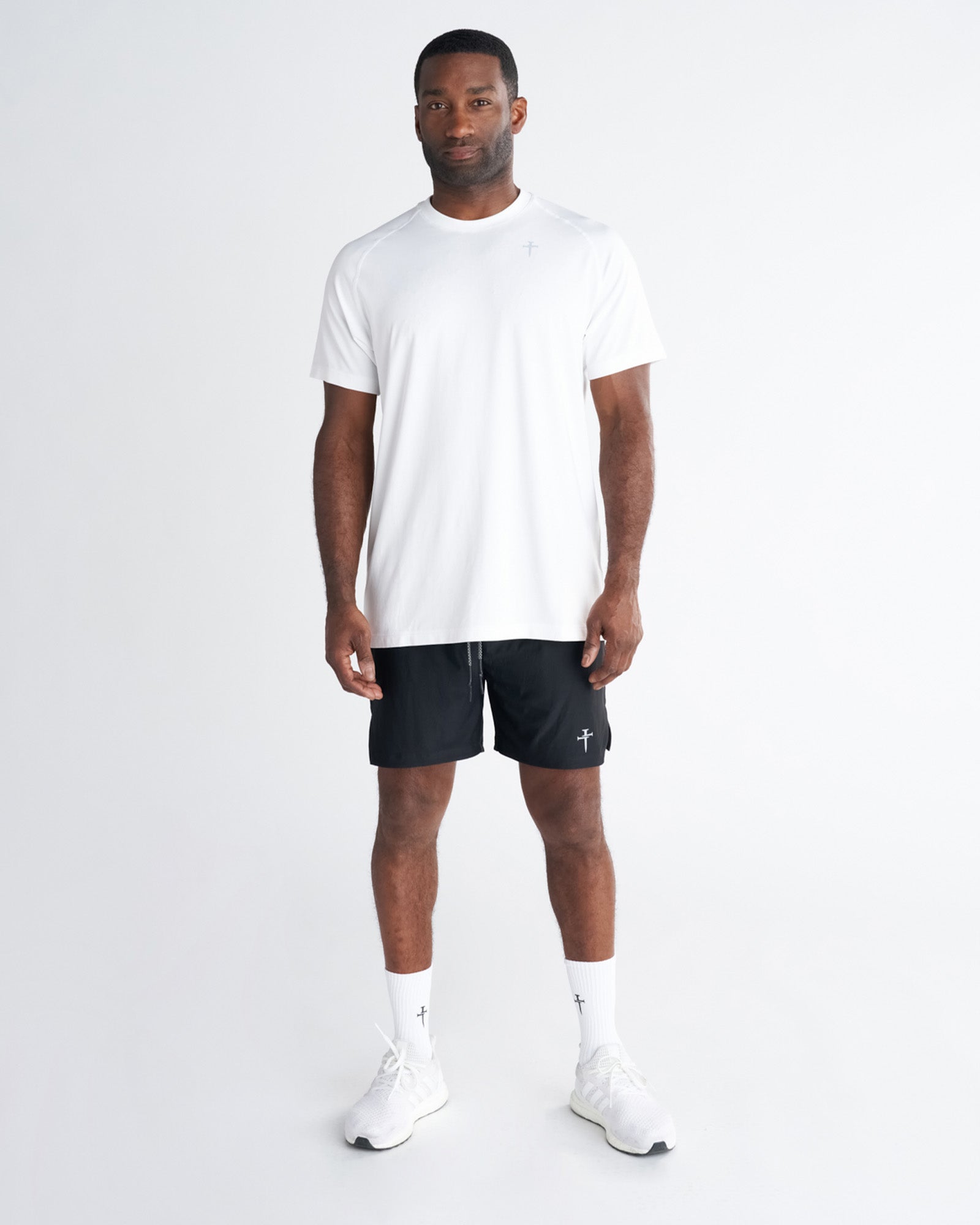 Man wearing the Core Tee in white, front view, paired with black shorts and white sneakers.