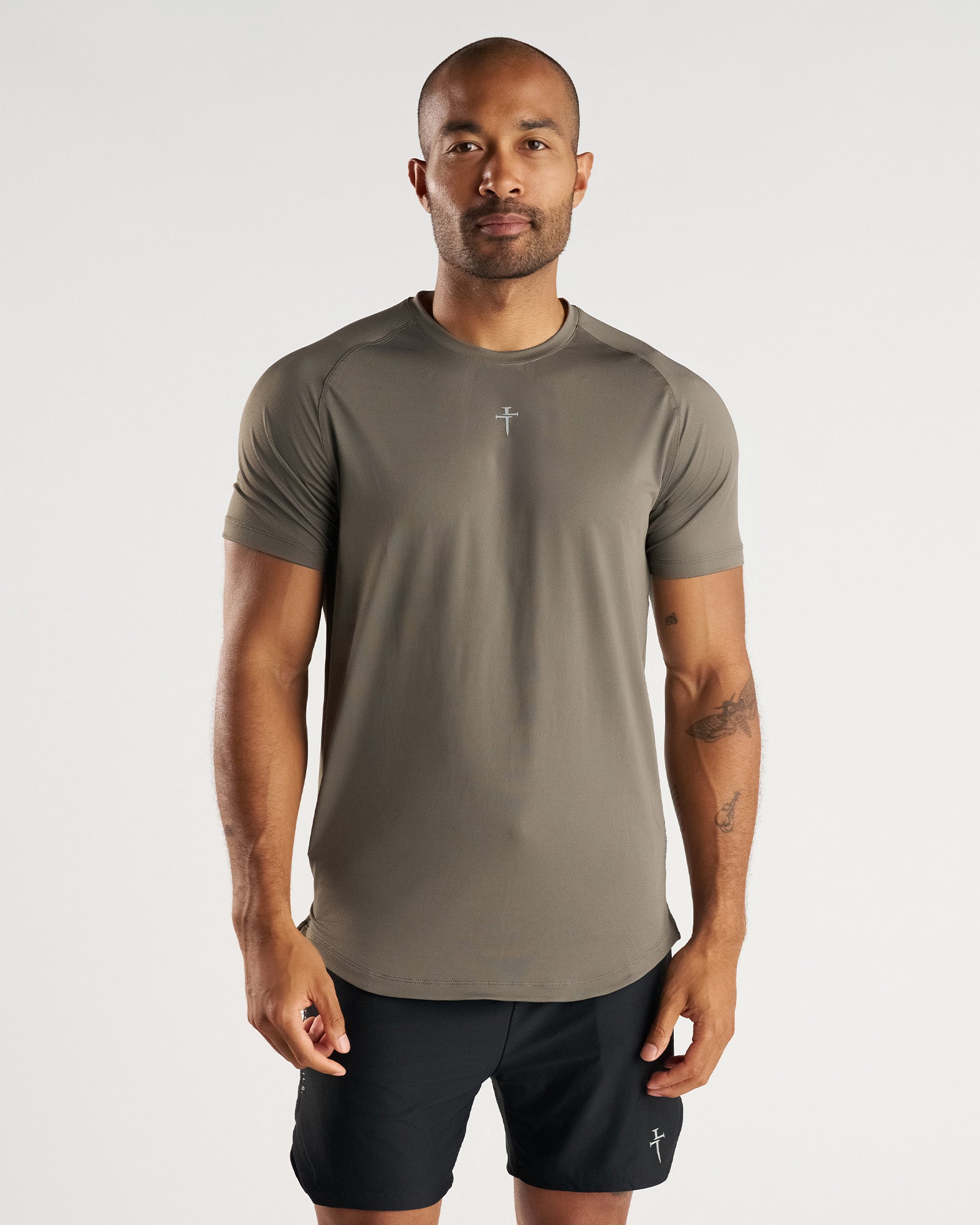 Man wearing Pro-Tech Tee Cross in Sage, front view, fitted athletic shirt with cross logo and black shorts.